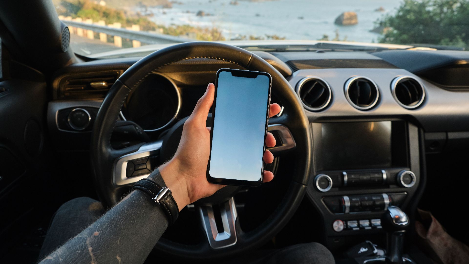 Crop anonymous guy with tattoo on hand navigating on mobile phone while driving car near sea