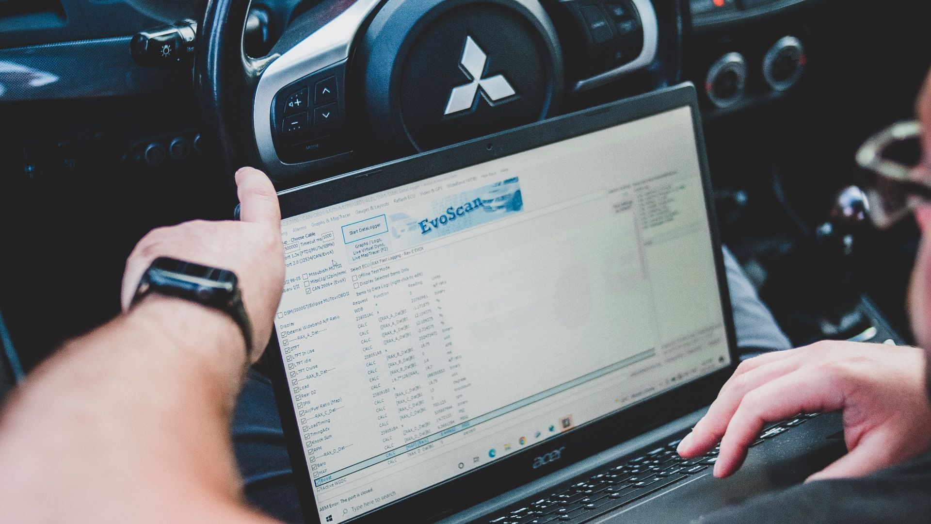 A person using a laptop inside a car for vehicle diagnostics, showcasing technology integration in automotive settings.