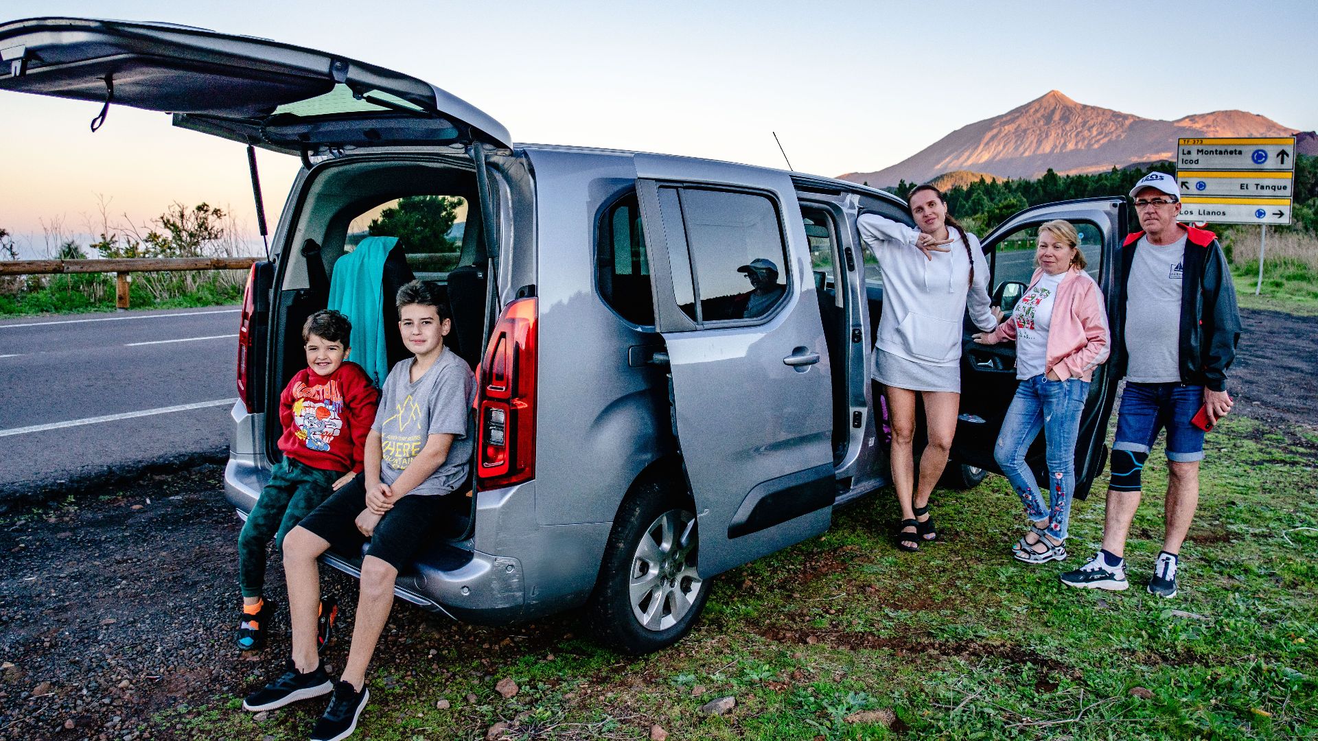 A family enjoys a scenic road trip by Mount Teide, Spain, with a van parked by the roadside.