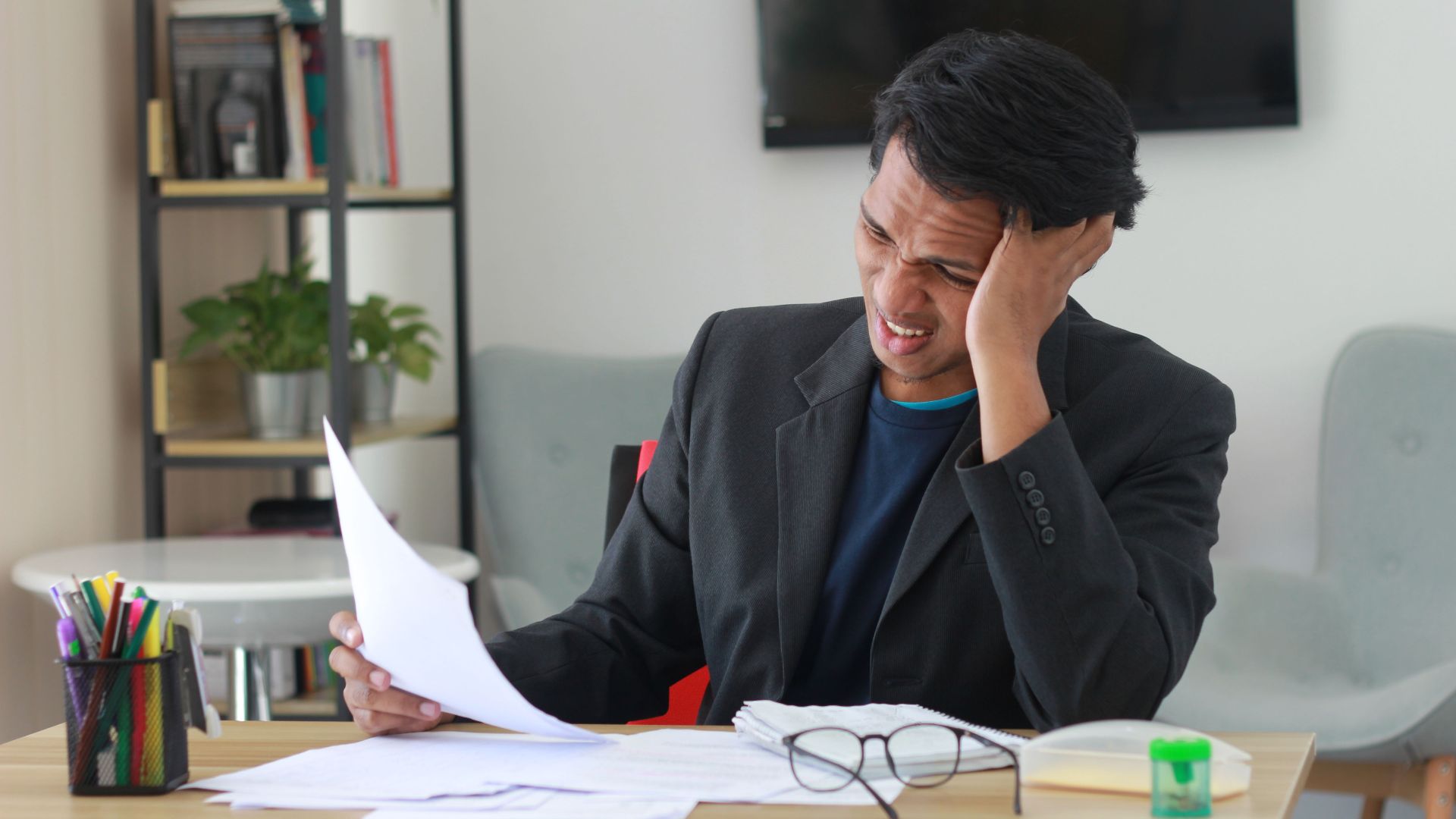 A businessman in an office experiencing stress while reviewing documents.