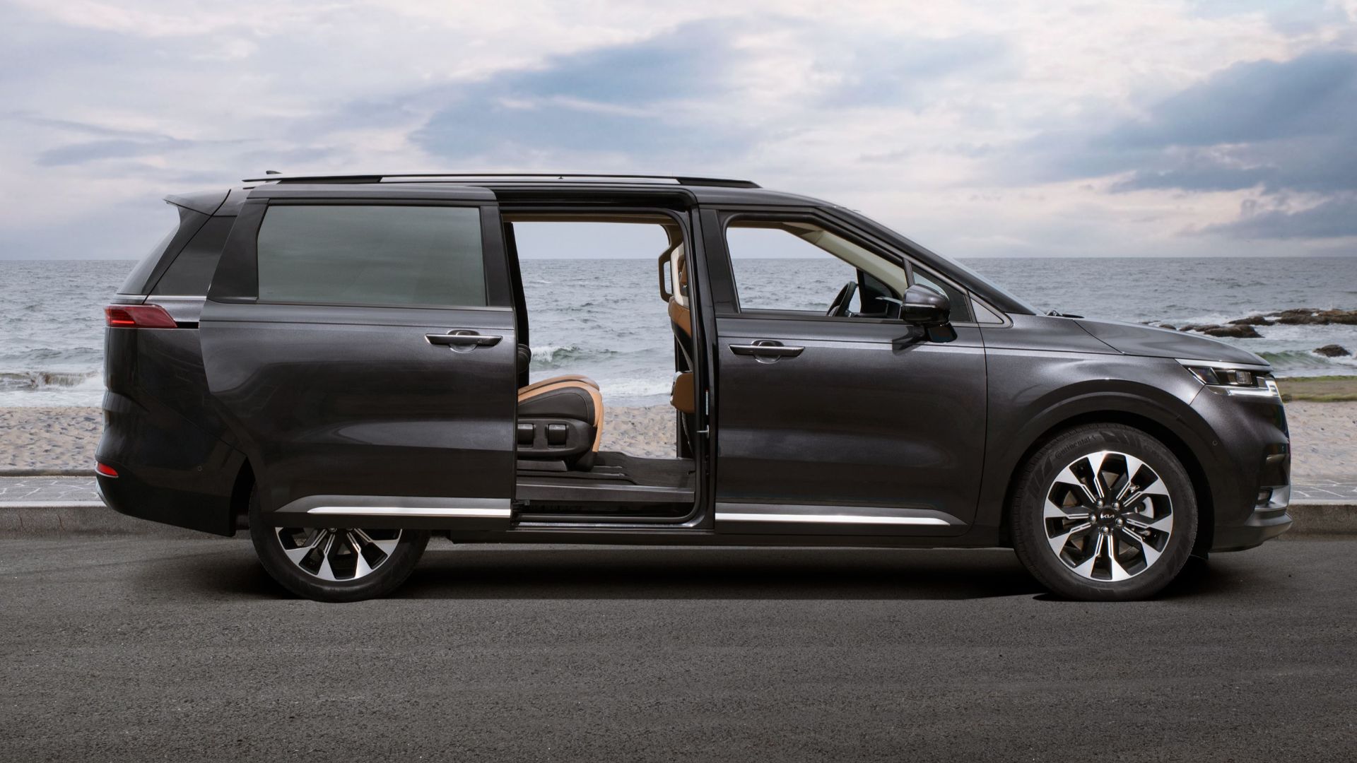Black SUV with open door parked by the ocean under a cloudy sky.