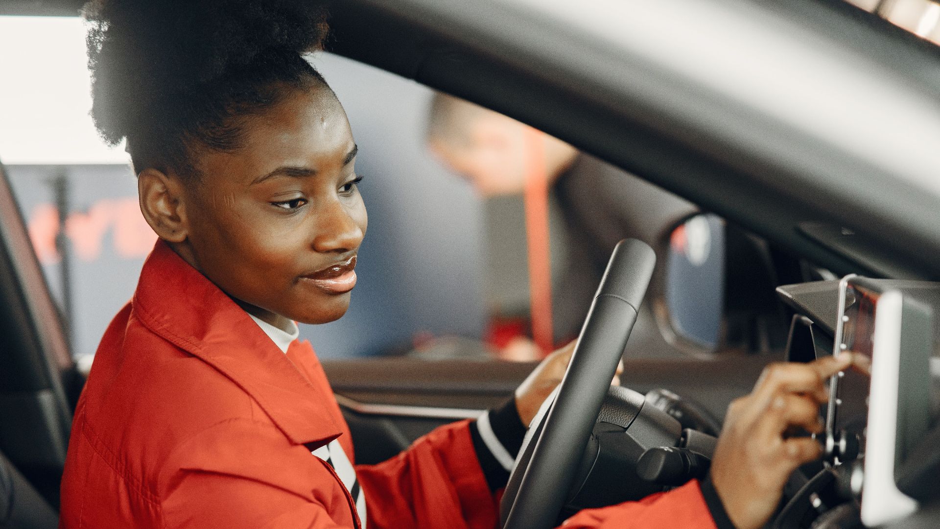 Young woman in red coat using touch screen in car interior.
