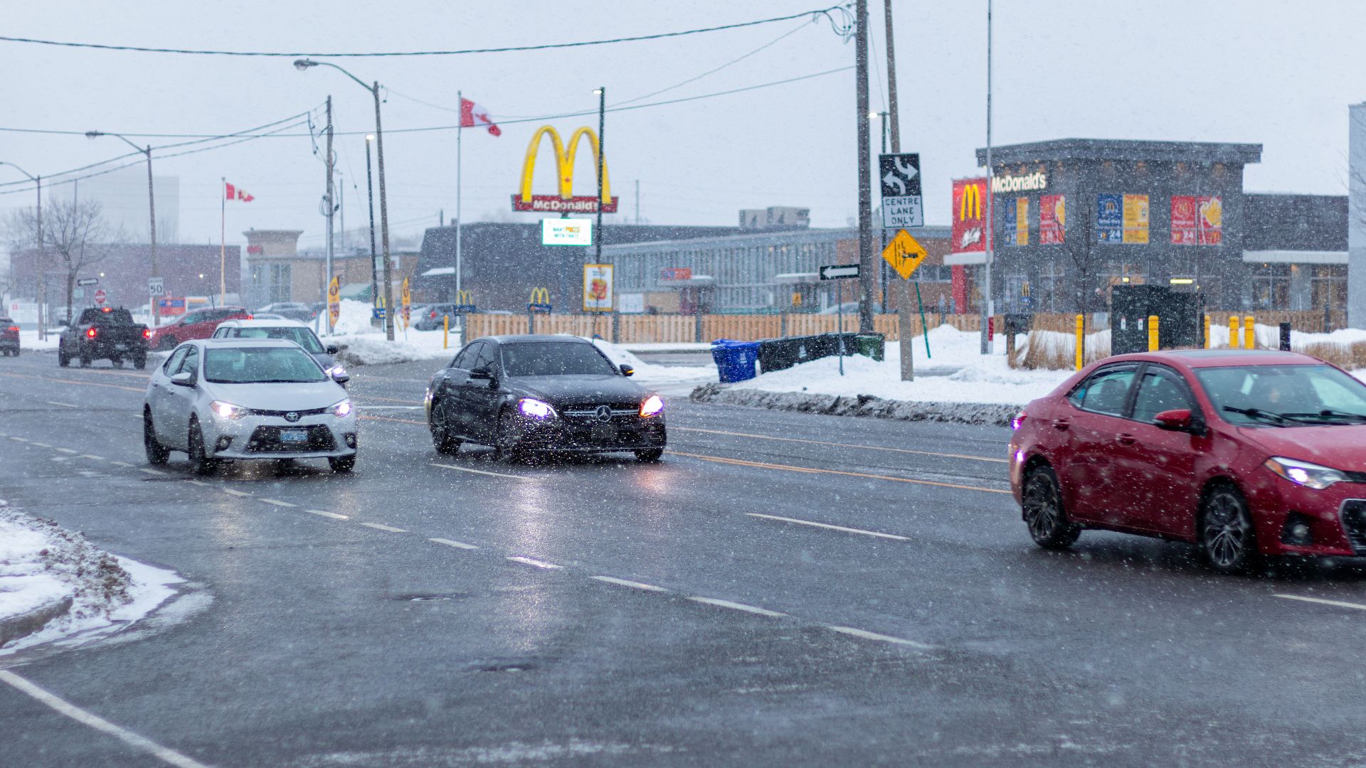 Winter street scene in Toronto with cars driving past McDonald's during snowfall.