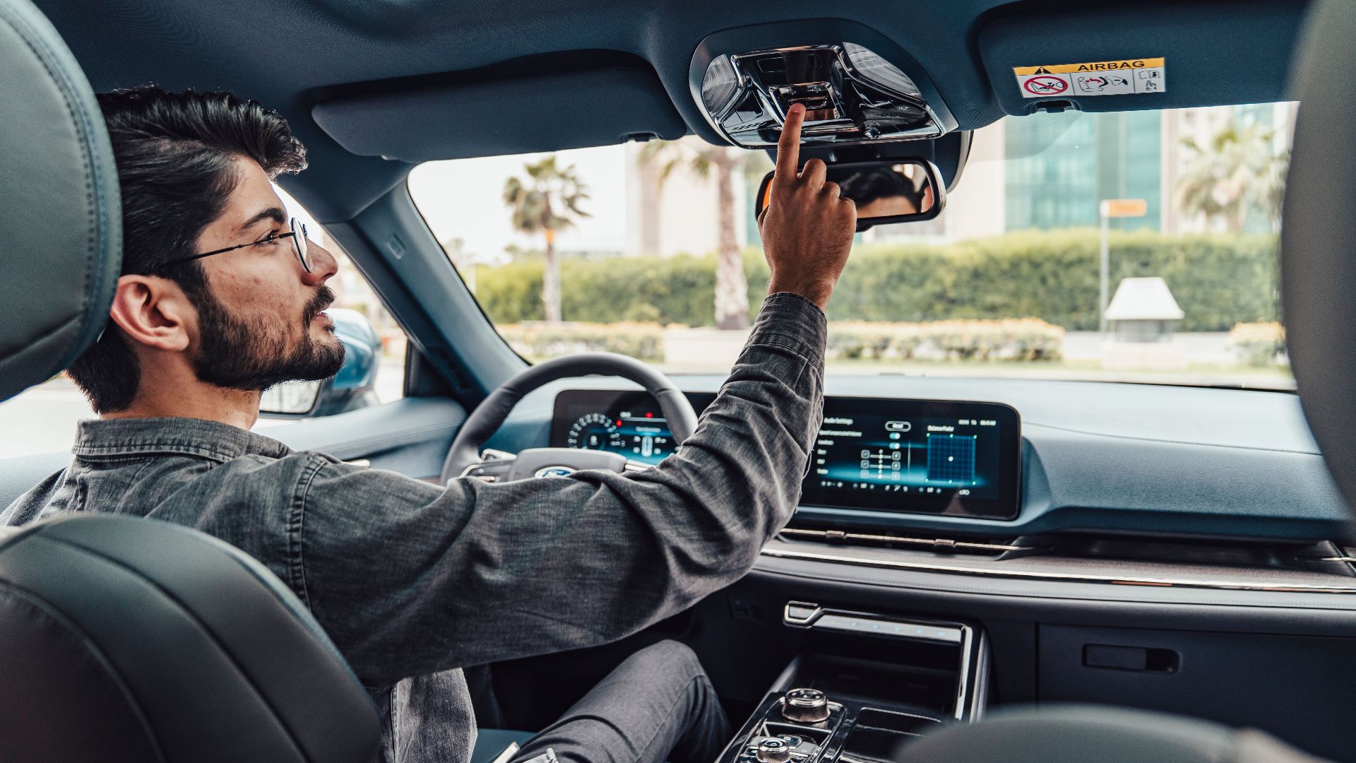 A man adjusts the interior features of a modern car while driving in Erbil, Iraq.