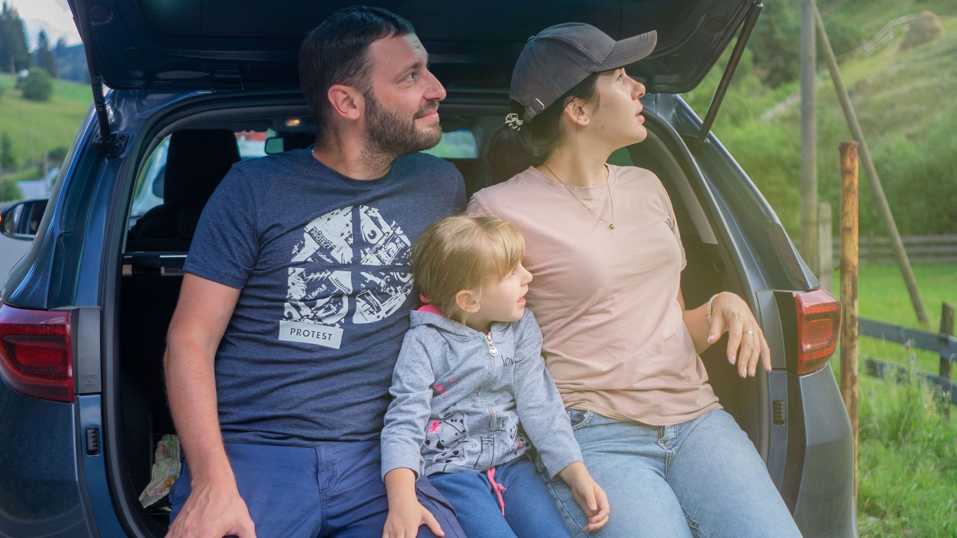 A family sits in a car trunk, enjoying an outdoor adventure in a scenic countryside.