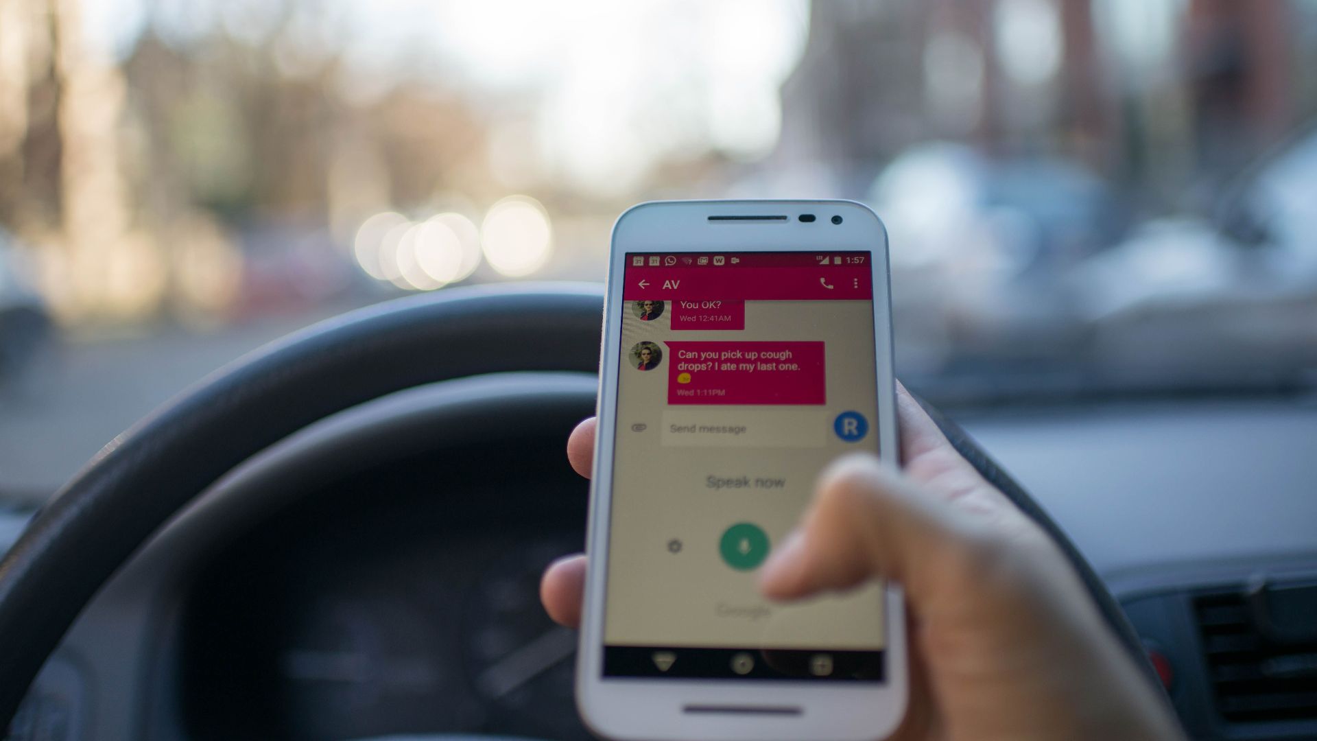 A person texting on a smartphone while driving an automobile in a city, illustrating distracted driving and technology use.