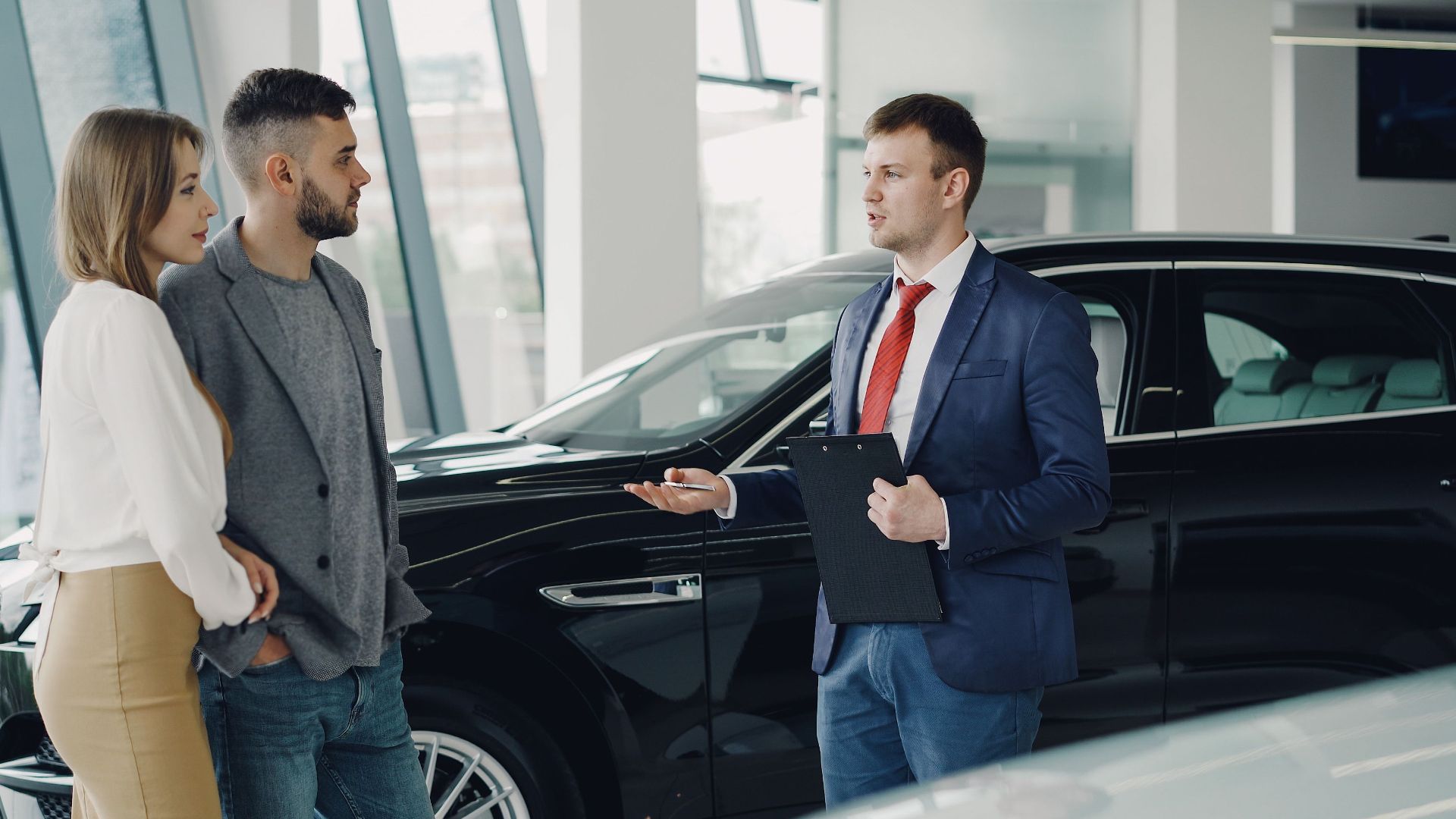 A couple talks with a salesman in a modern car showroom, considering a vehicle purchase.