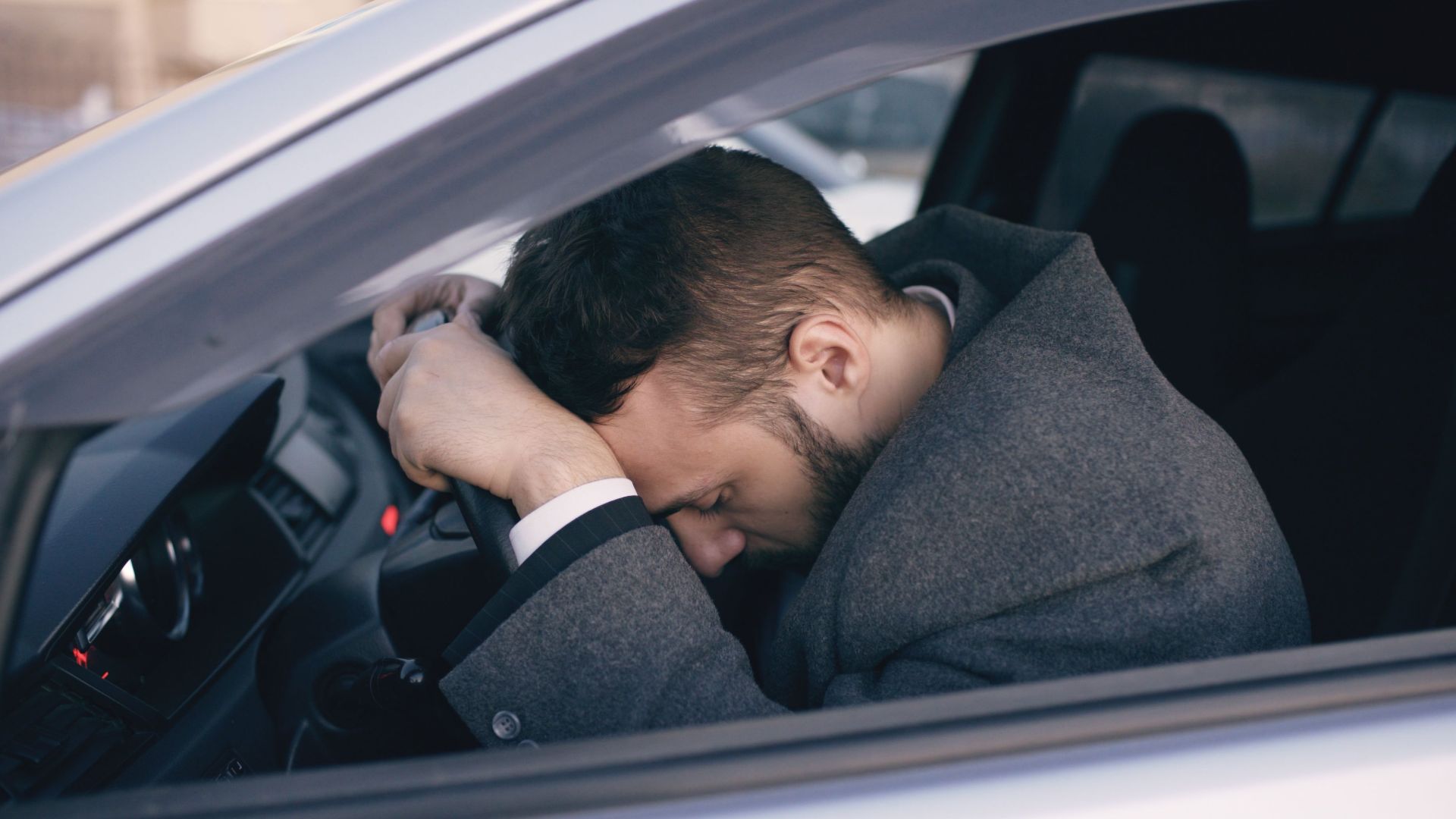 Man in car showing stress with head on steering wheel, highlighting emotional fatigue.