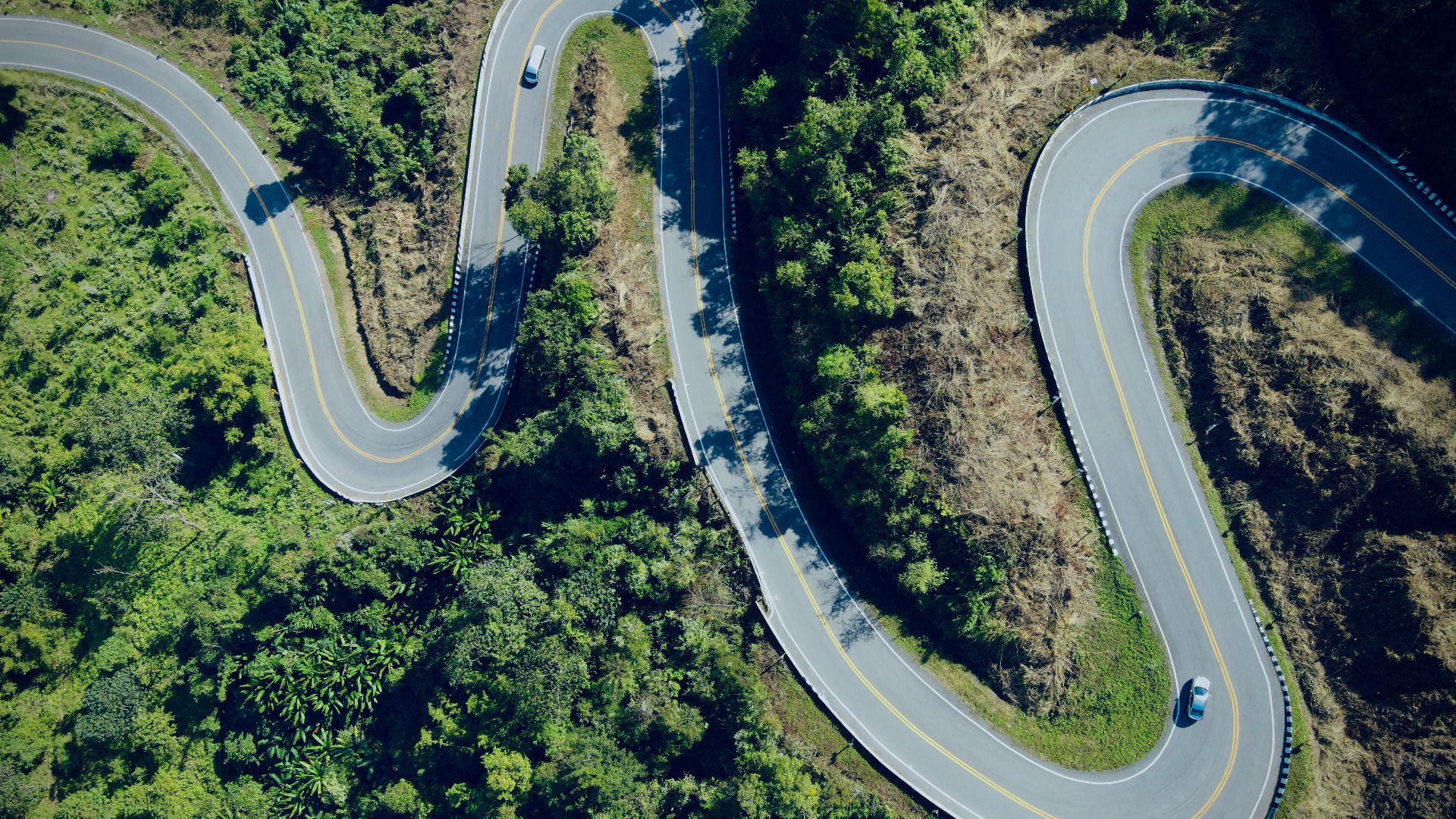 Aerial view of a winding road through lush forest in Thailand, capturing nature's beauty.