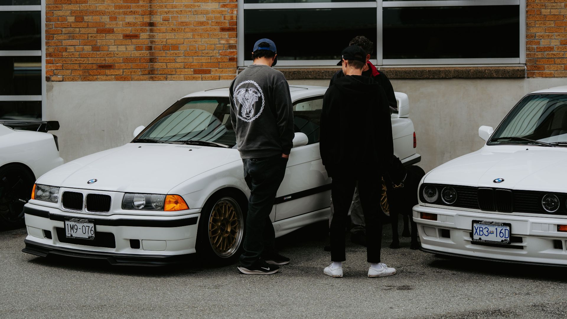 Two individuals standing by classic white BMWs in an urban setting.