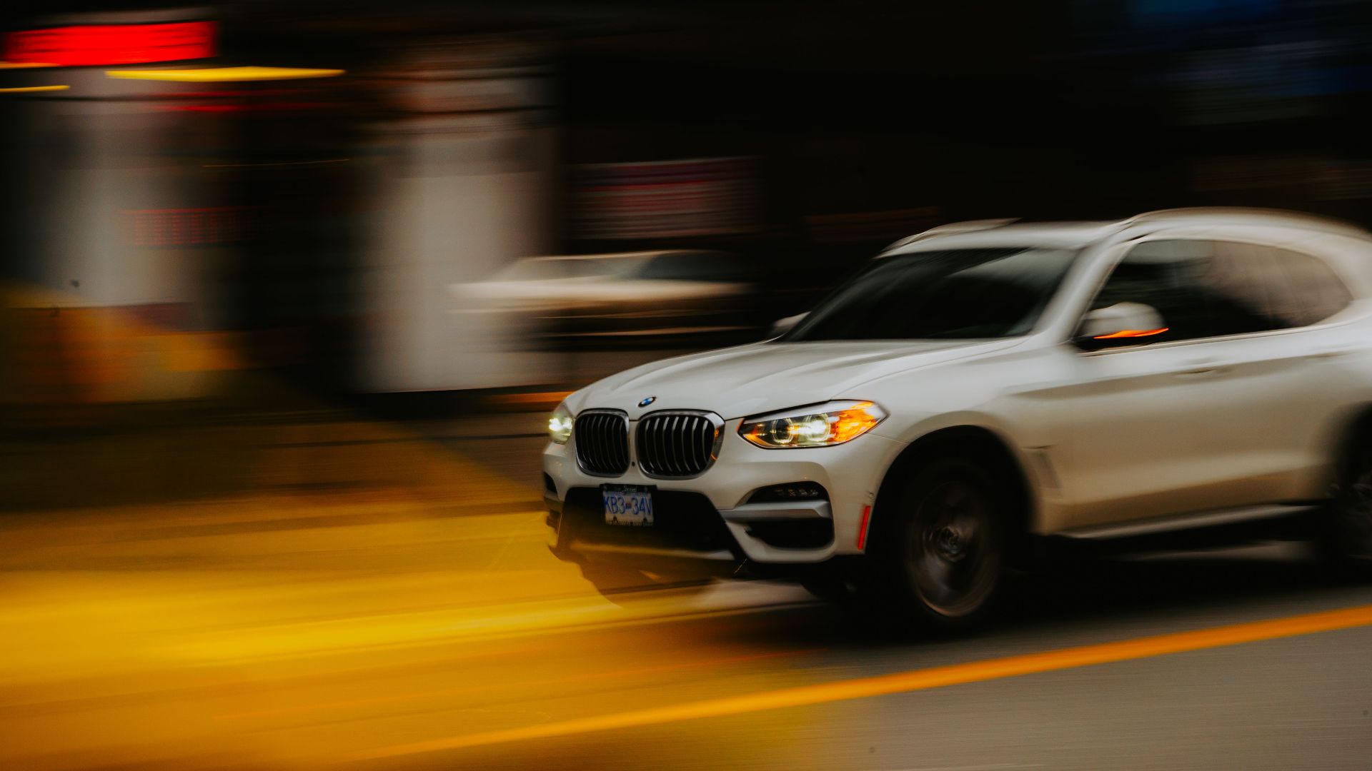 Blurred motion shot of a white BMW SUV speeding through urban city streets.