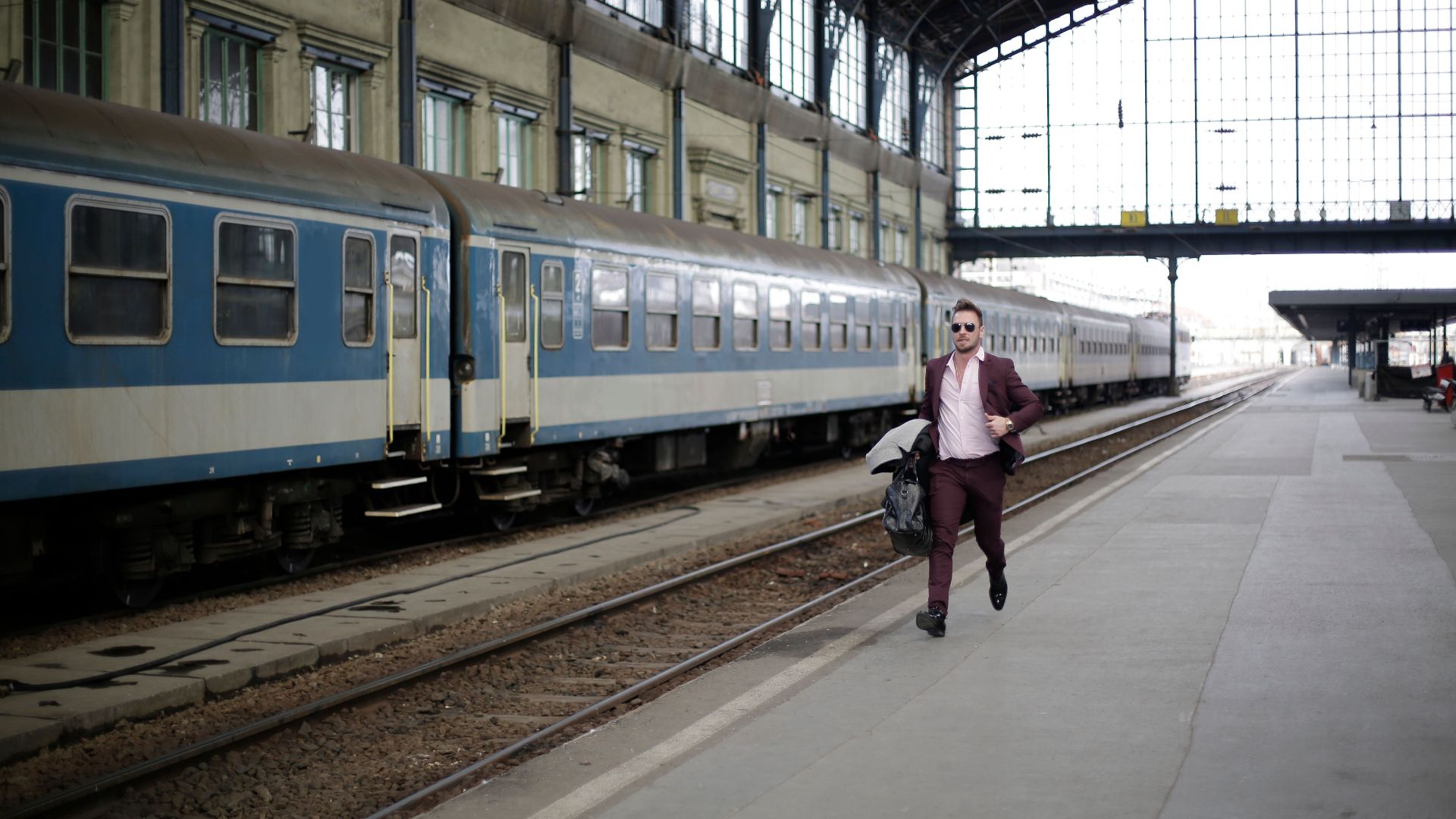 A businessman in a purple suit runs on a railway platform, rushing to catch a train during daylight.