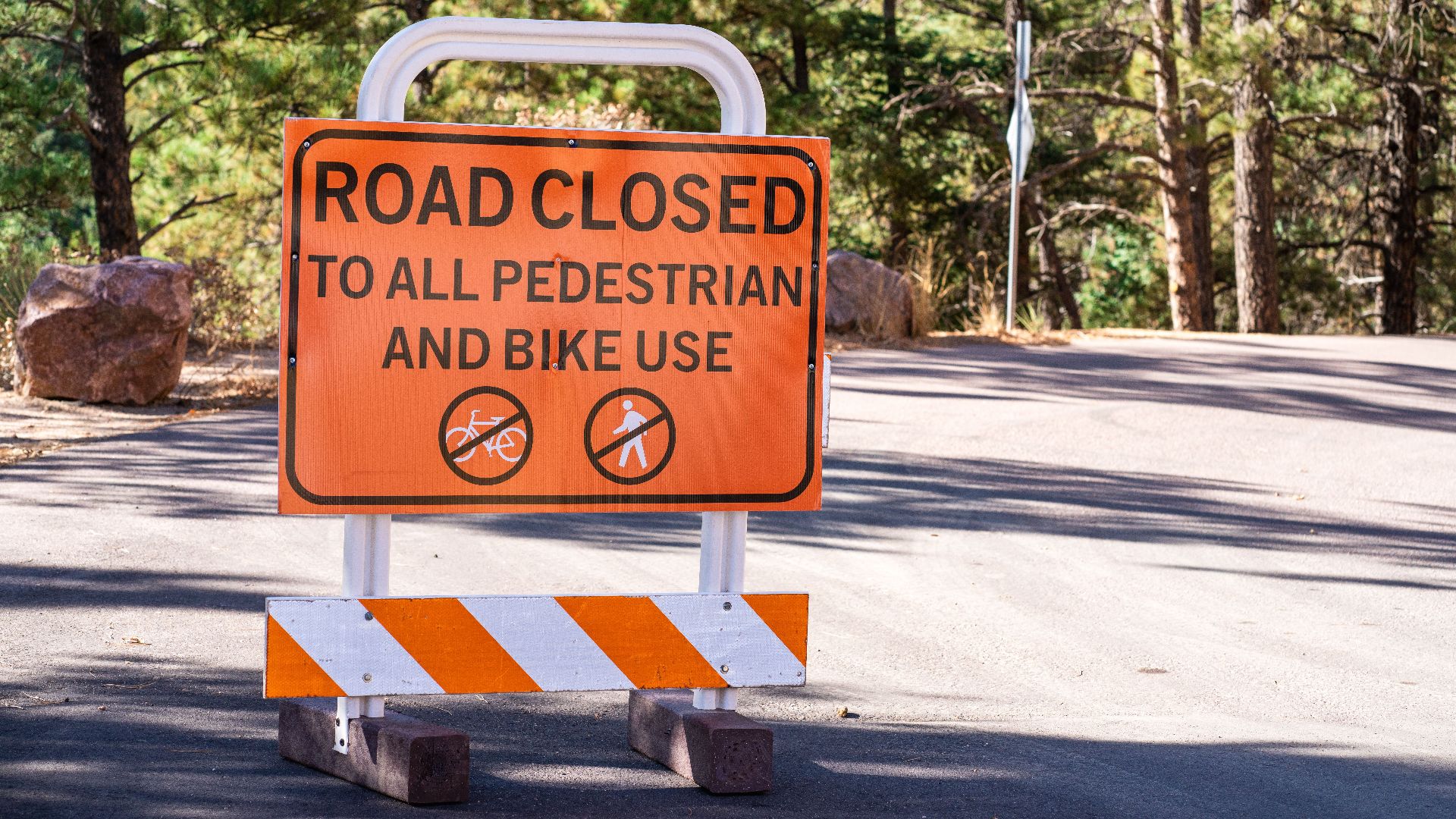 Bright road closed sign restricting pedestrian and bike access amidst forest backdrop.