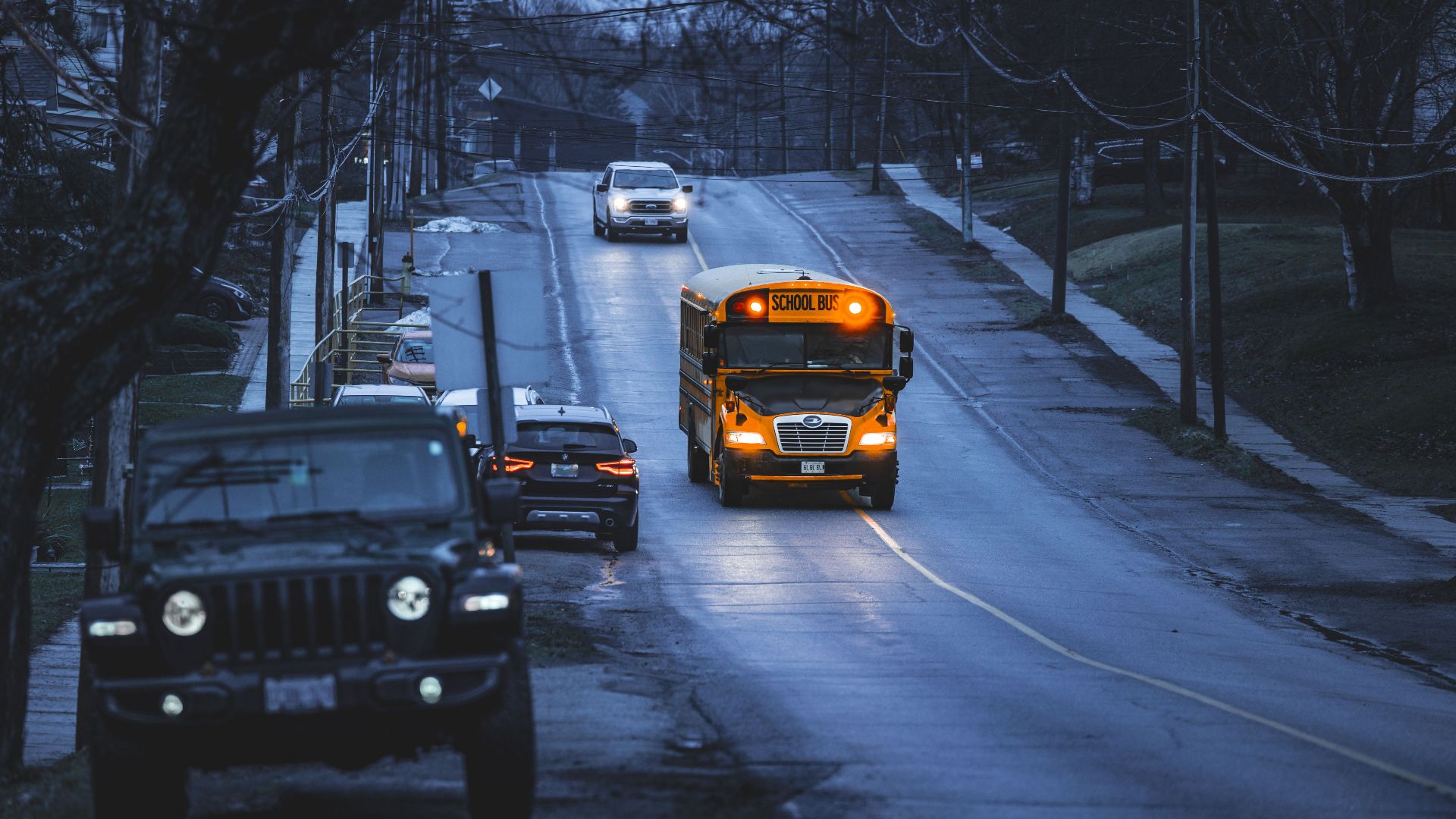 Yellow school bus on a quiet road, early morning commute scene with vehicles.
