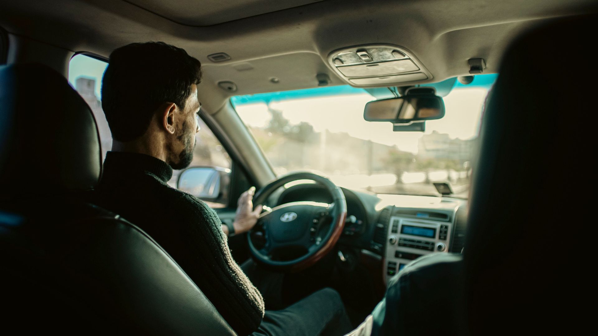 Man driving through city streets of Manbij, Aleppo, in a modern sedan.