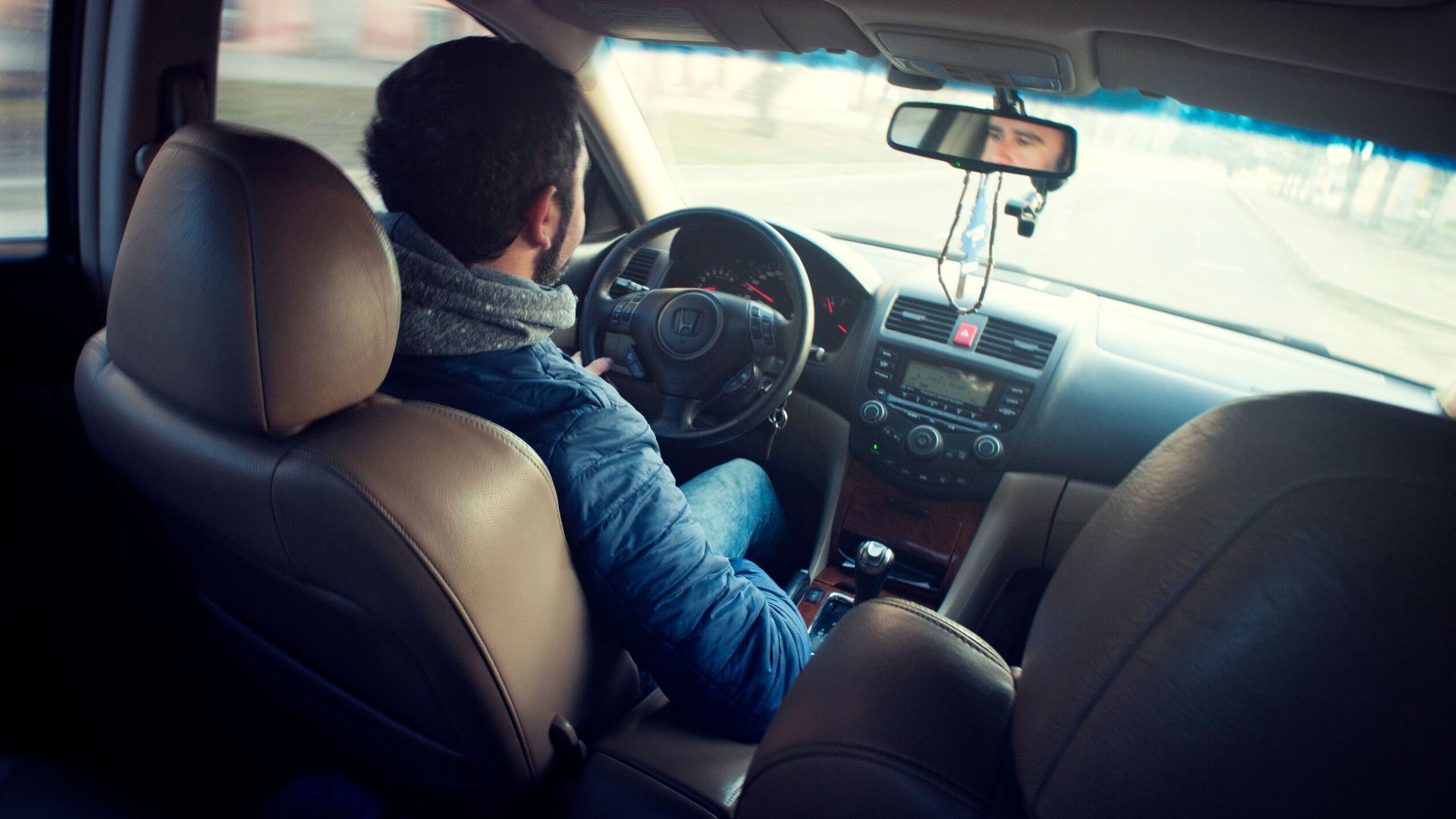 A man driving a car with focus on interior, dashboard, and steering wheel, captured from the backseat.
