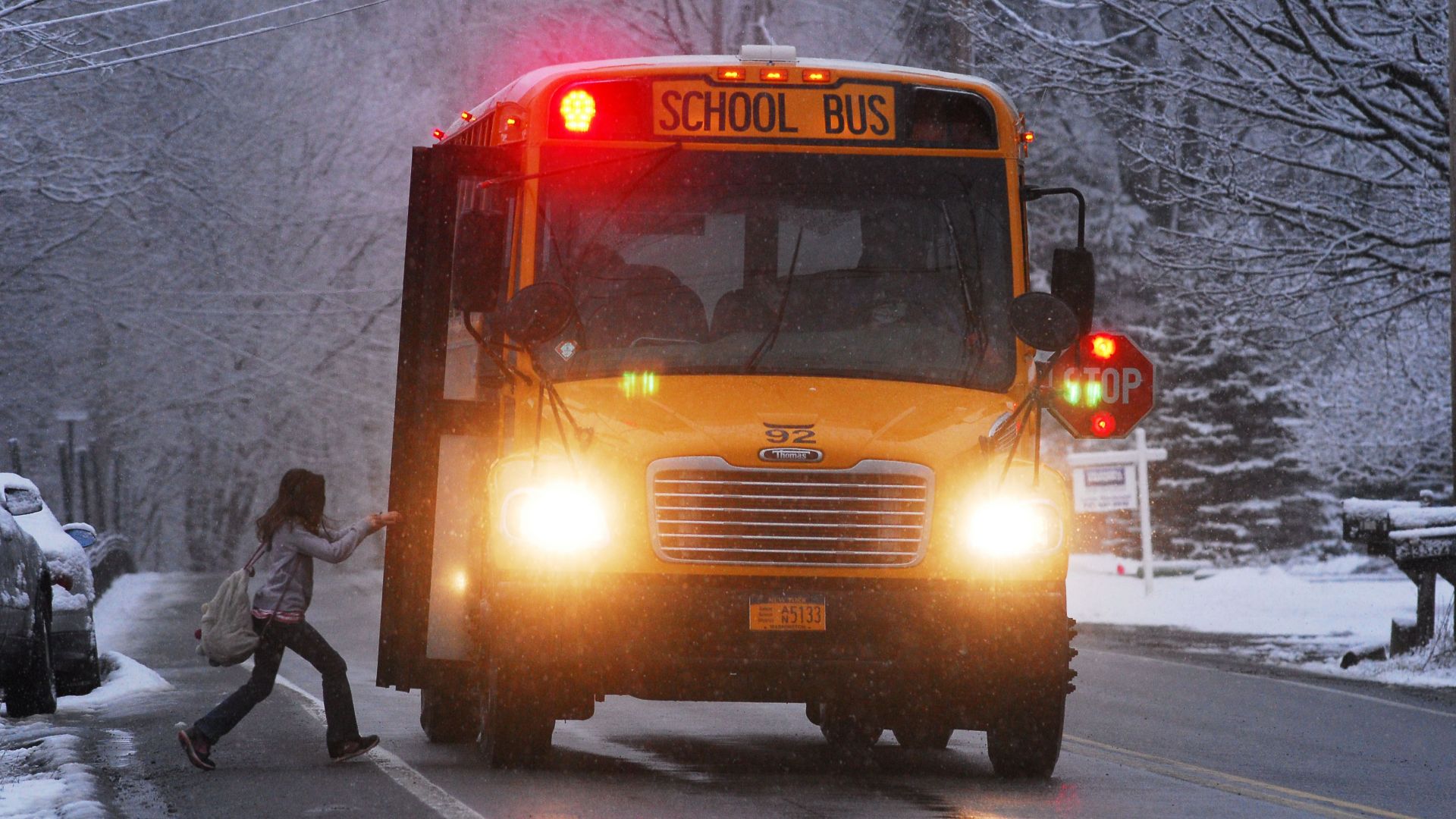 A school bus on a snowy road with a child boarding in winter conditions.
