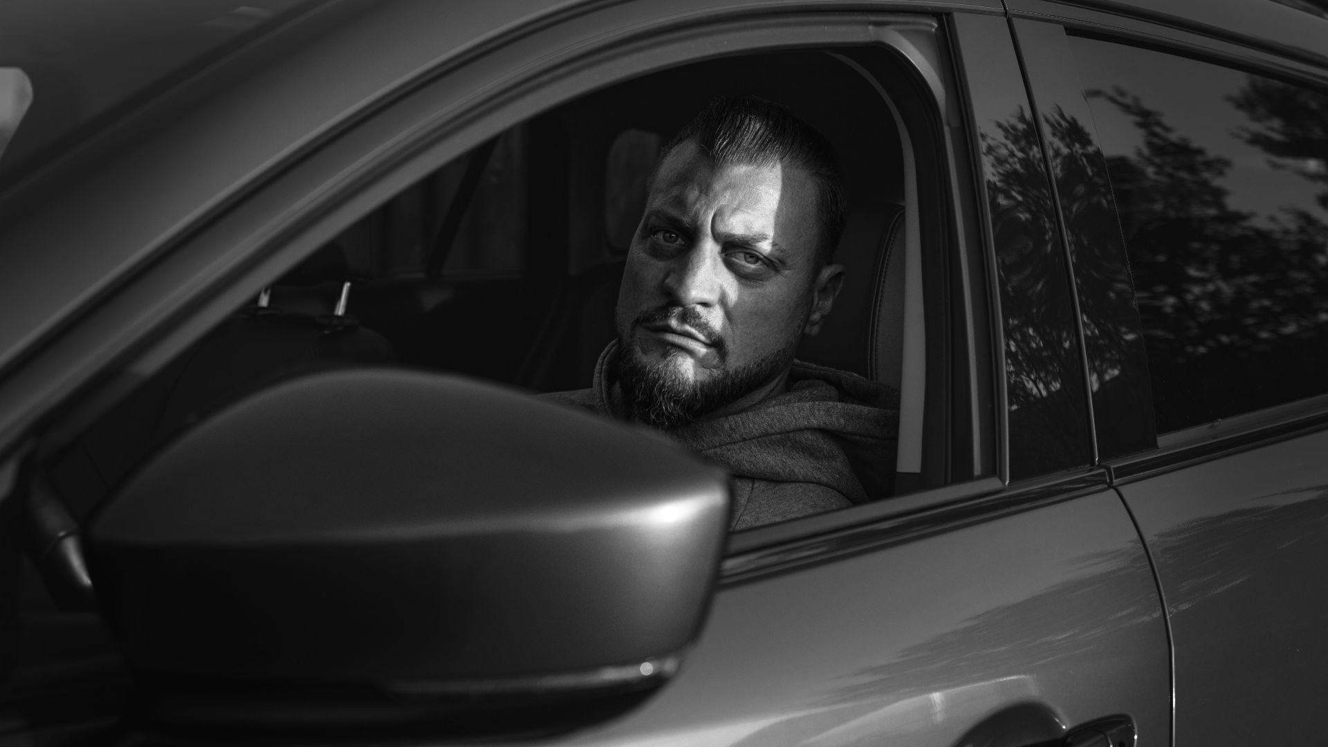 Serious bearded man looking out from a vehicle in a monochrome setting.