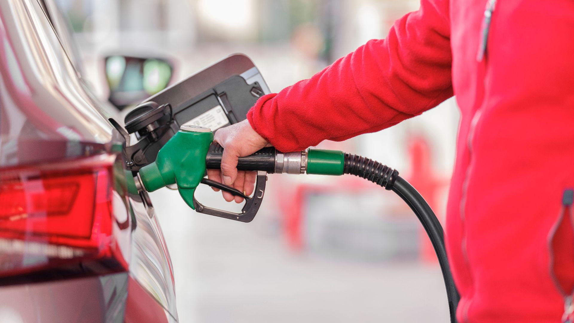 Close-up of a person refueling a car with a green hose at a gas station.