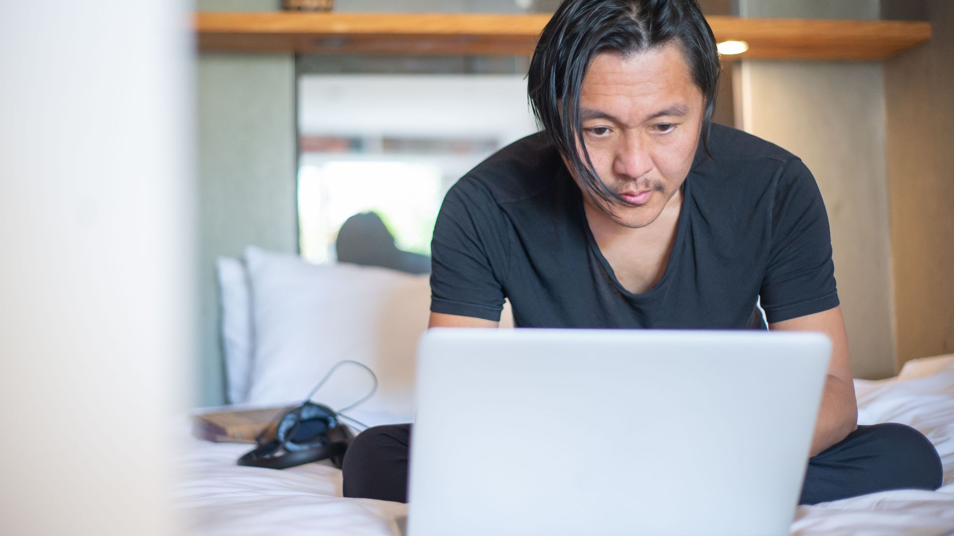 An Asian man working from home on a laptop, focusing on his digital tasks in a cozy indoor setting.
