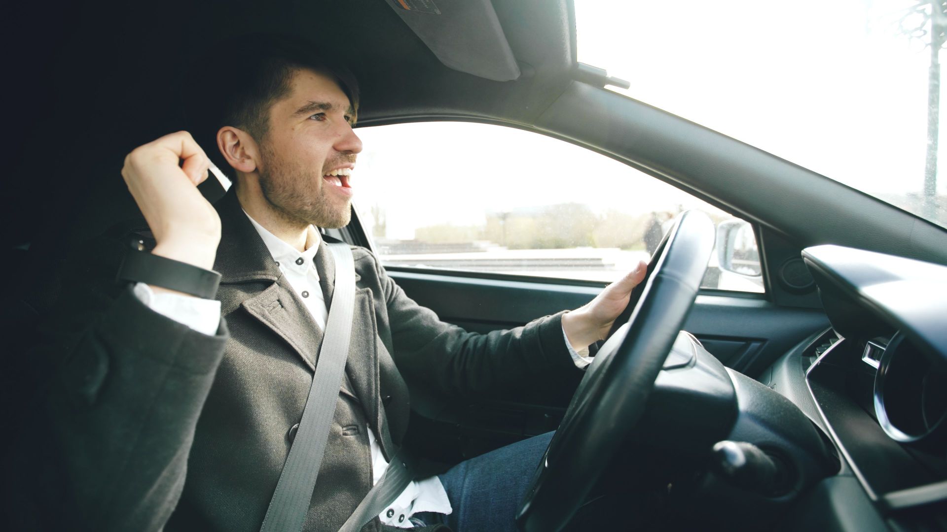 Cheerful adult male expressing joy while driving a car during daytime.