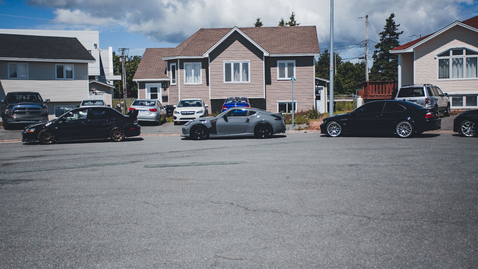 Sunny neighborhood street with modern homes and parked vehicles on a bright day.