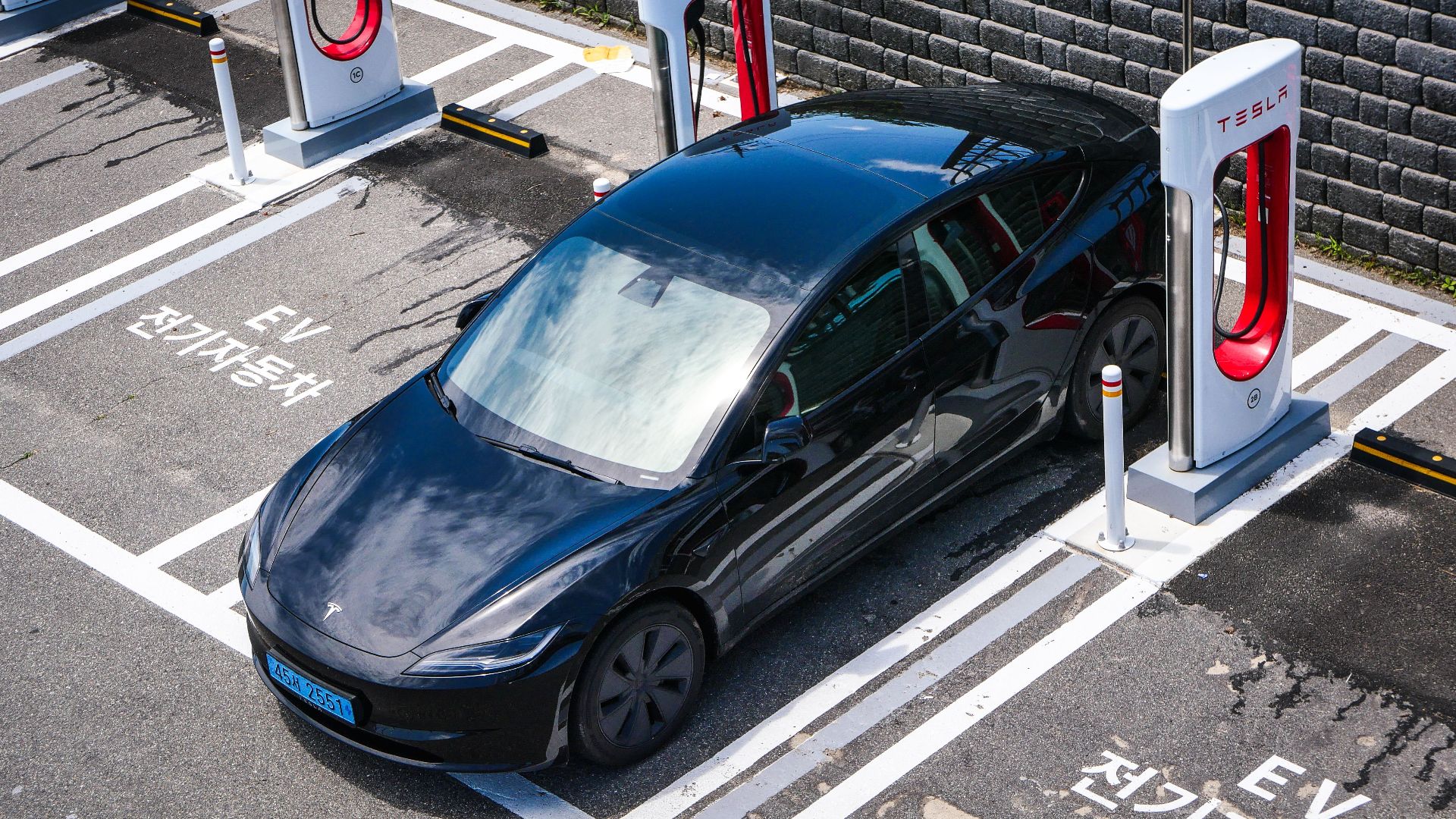 A black Tesla parked at a charging station in an urban setting.