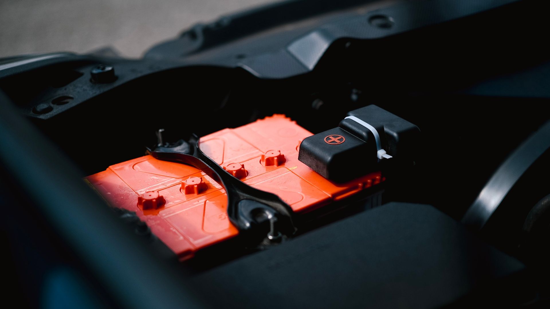 Detailed view of an orange car battery inside a vehicle's engine bay, highlighting its features.