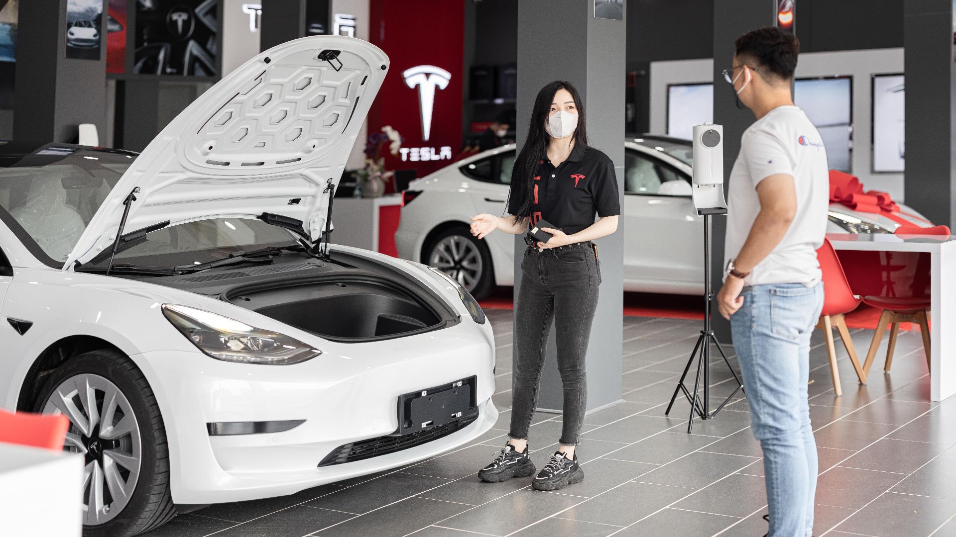 A customer talks with a sales representative about a Tesla Model 3 in a car dealership, showcasing the electric car's features.