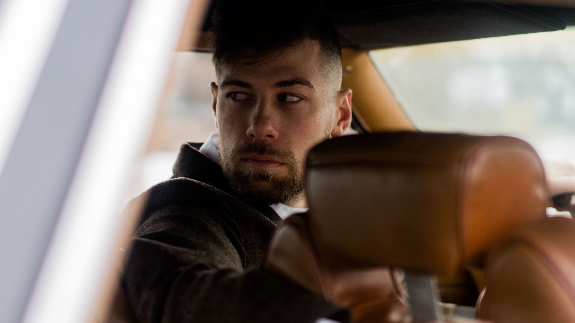 Confident adult male driver in elegant outfit sitting in vehicle while looking in back window on street in daytime