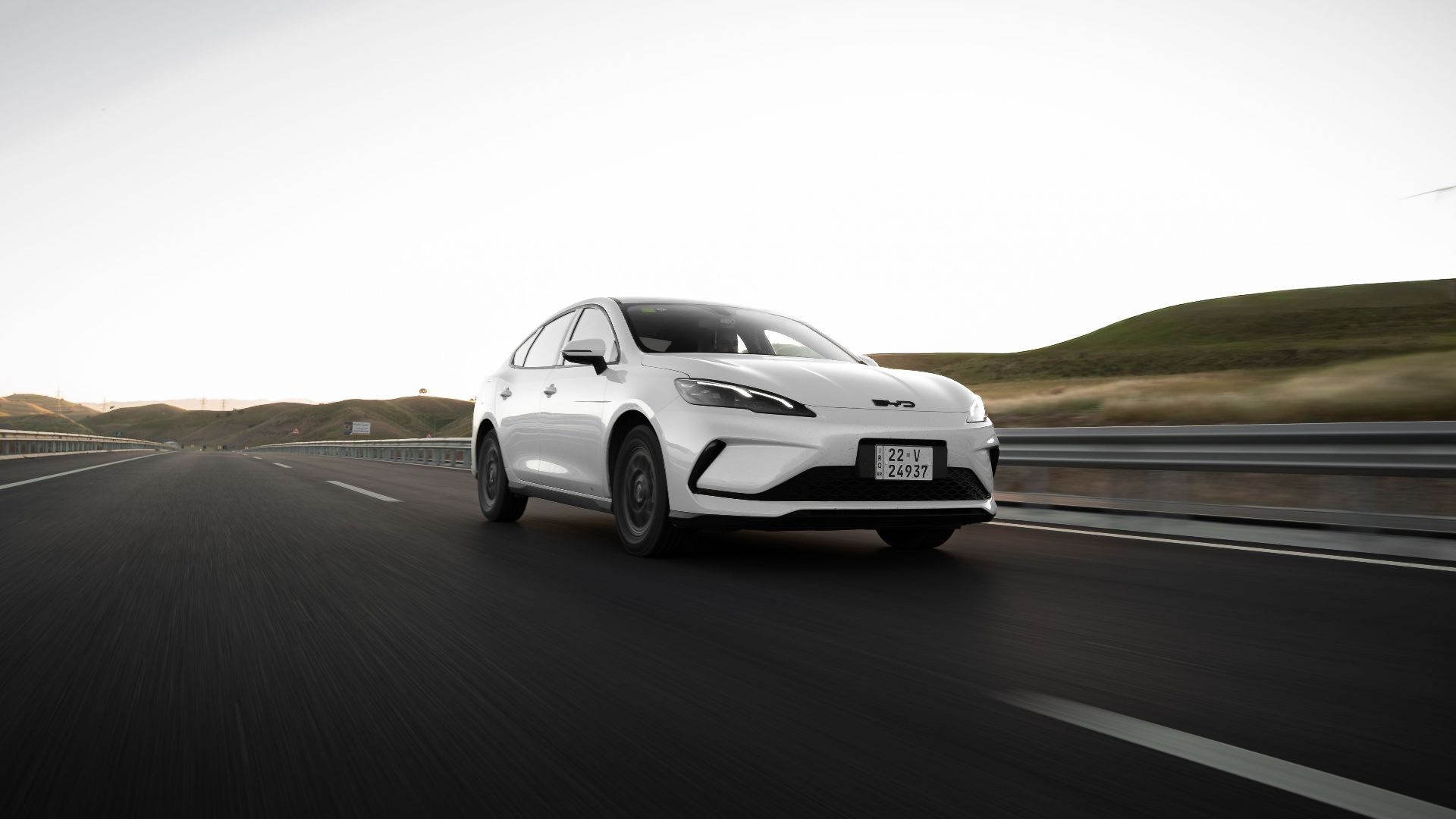 A modern white car drives on an open highway at dawn, highlighting sleek design and open road adventure.