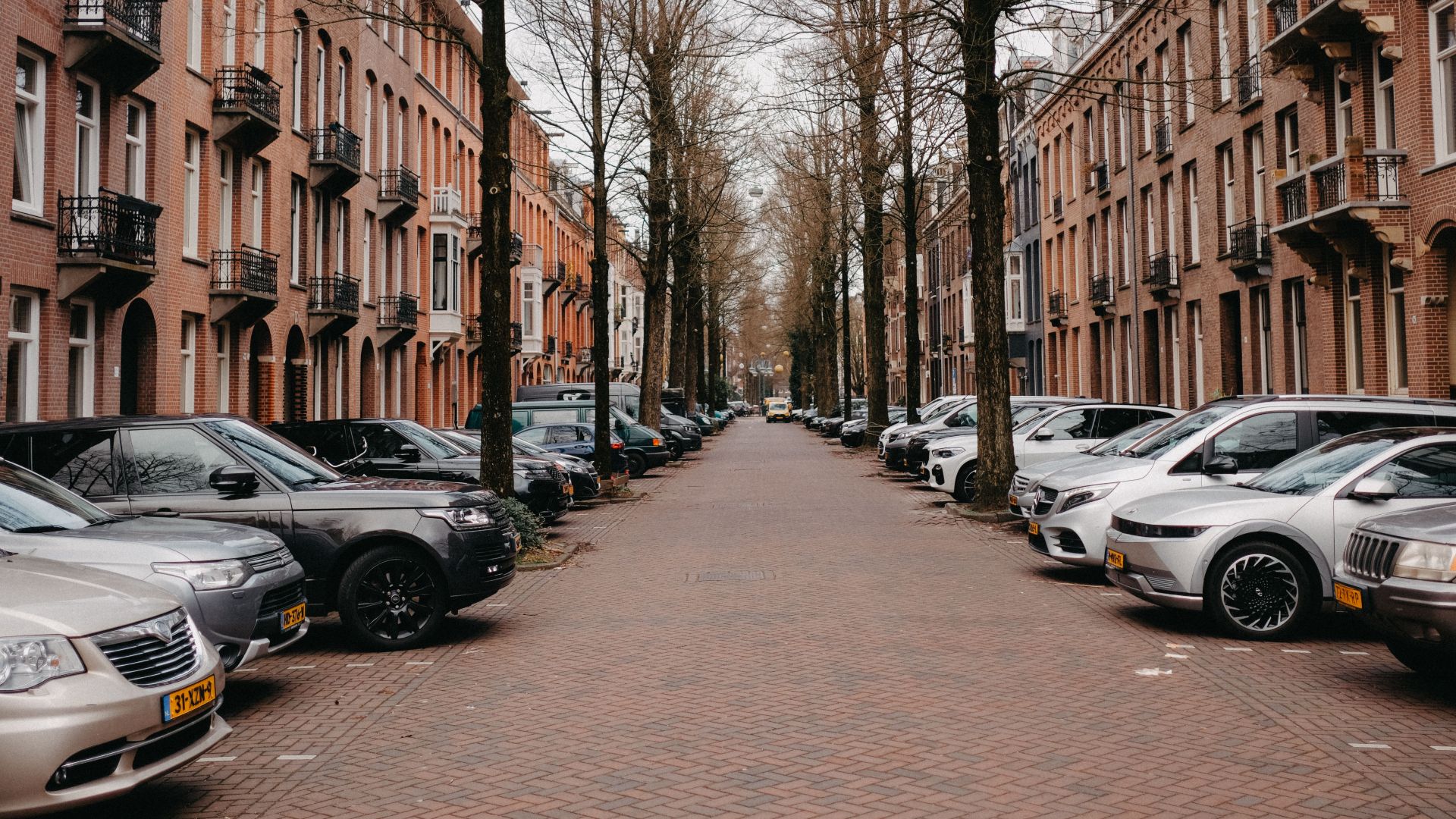 A picturesque Amsterdam street lined with brick buildings and parked cars, capturing urban charm.