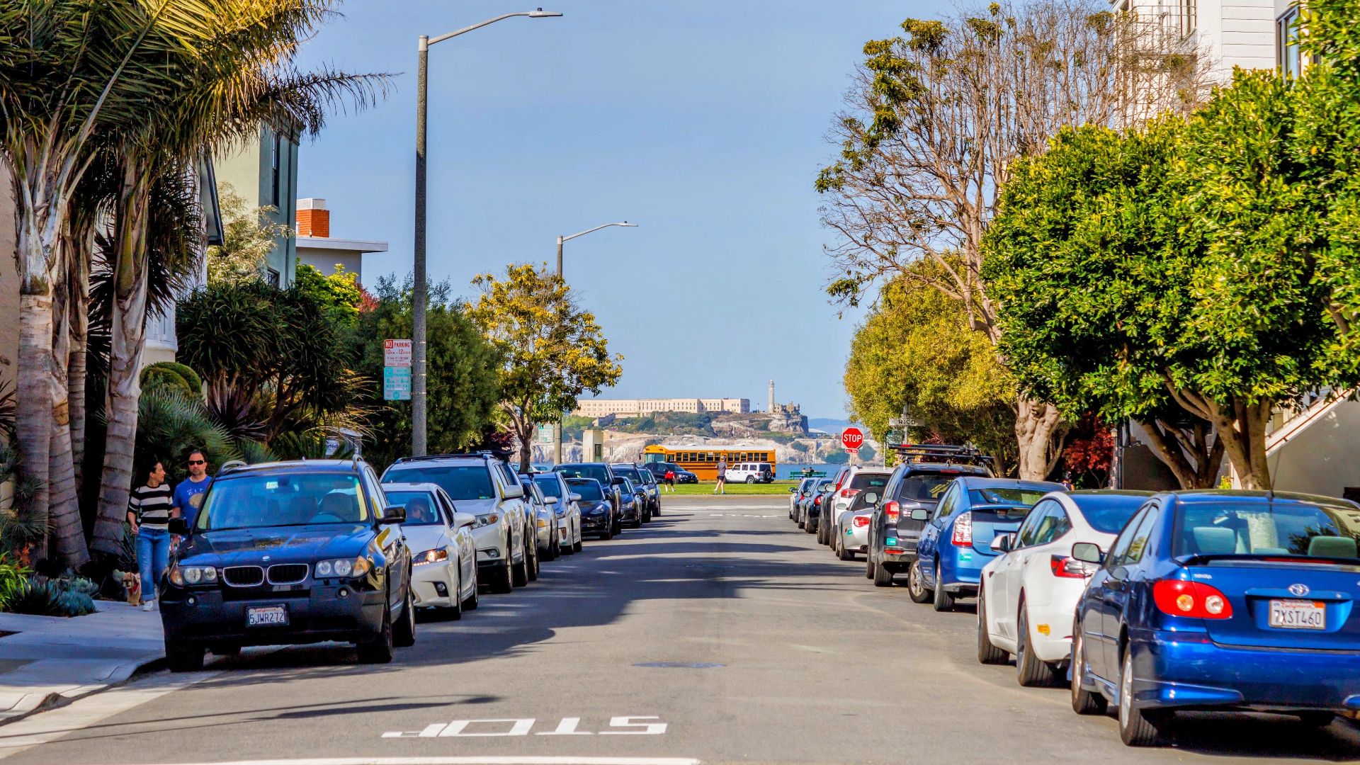 Street view with parked cars and Alcatraz Island in the distance.