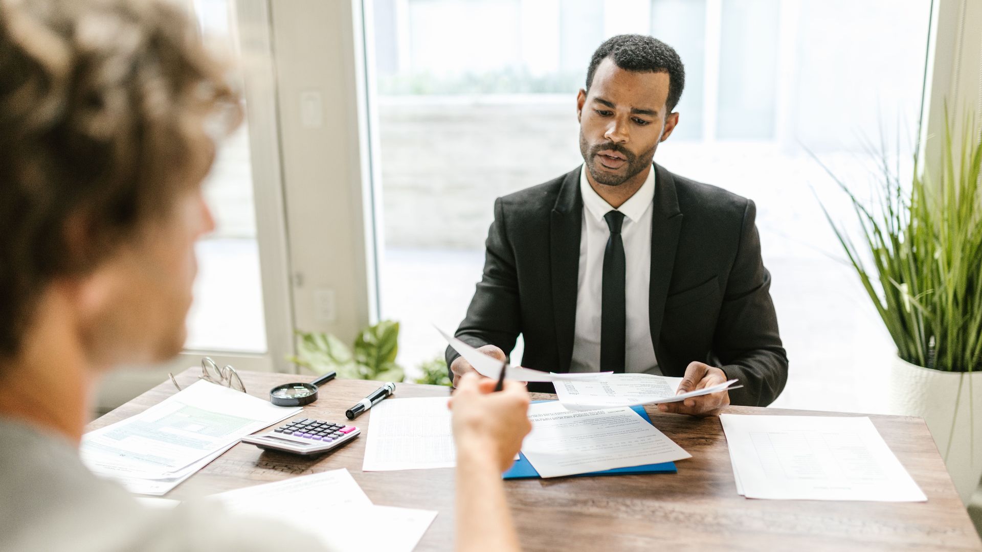 Businessman in a suit reviewing documents during a meeting indoors with a colleague.
