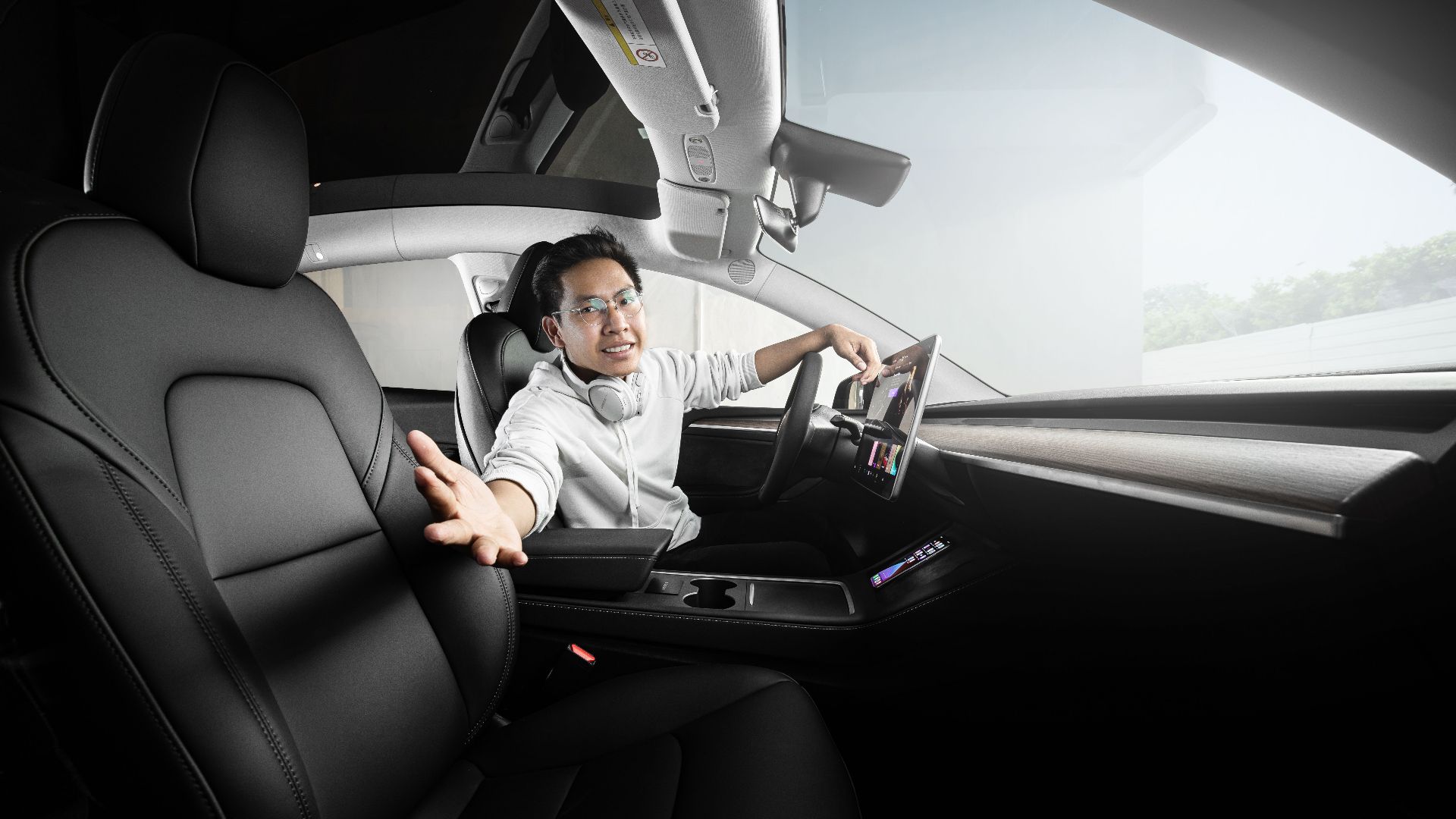 Man extends hand from modern car interior featuring touchscreen technology and sleek design.
