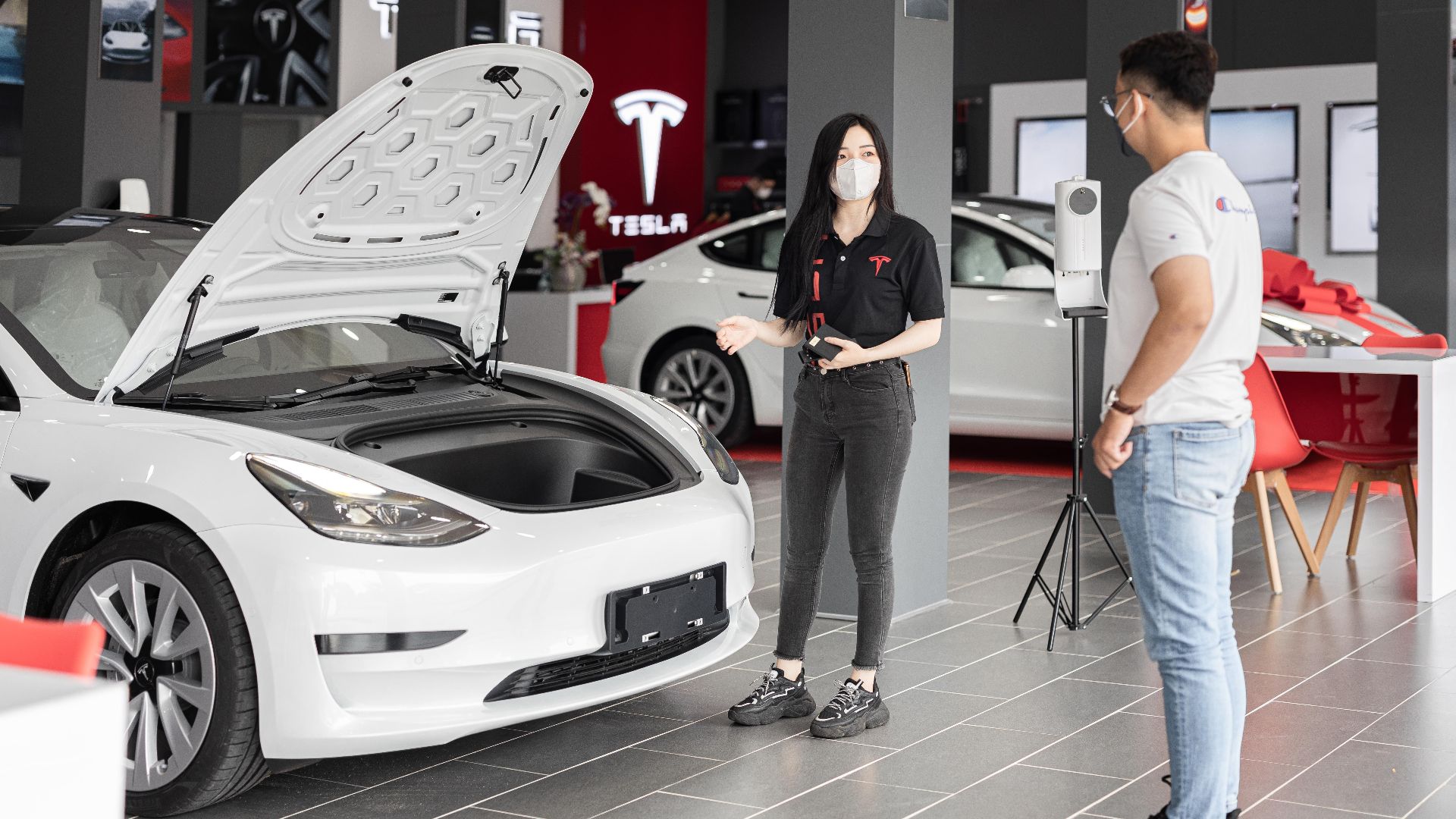A customer talks with a sales representative about a Tesla Model 3 in a car dealership, showcasing the electric car's features.