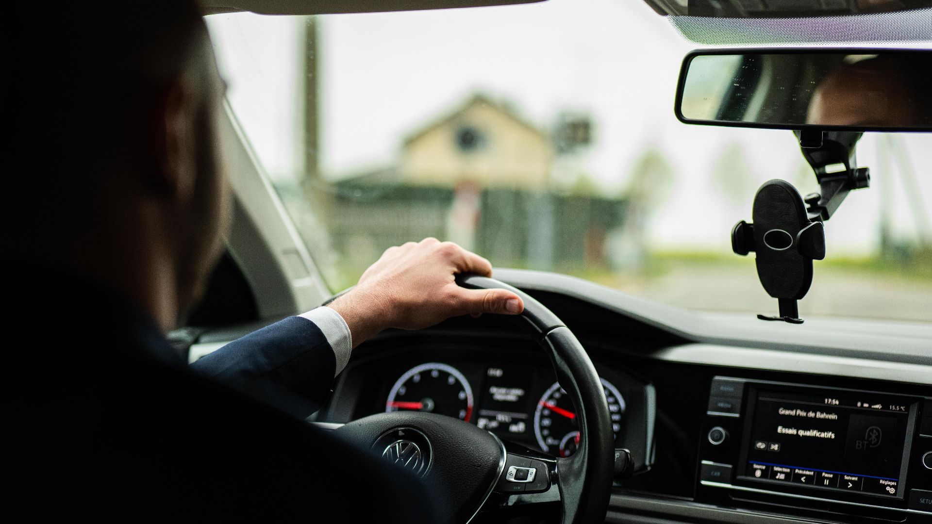 Businessman in suit driving a car, focus on steering wheel and dashboard.