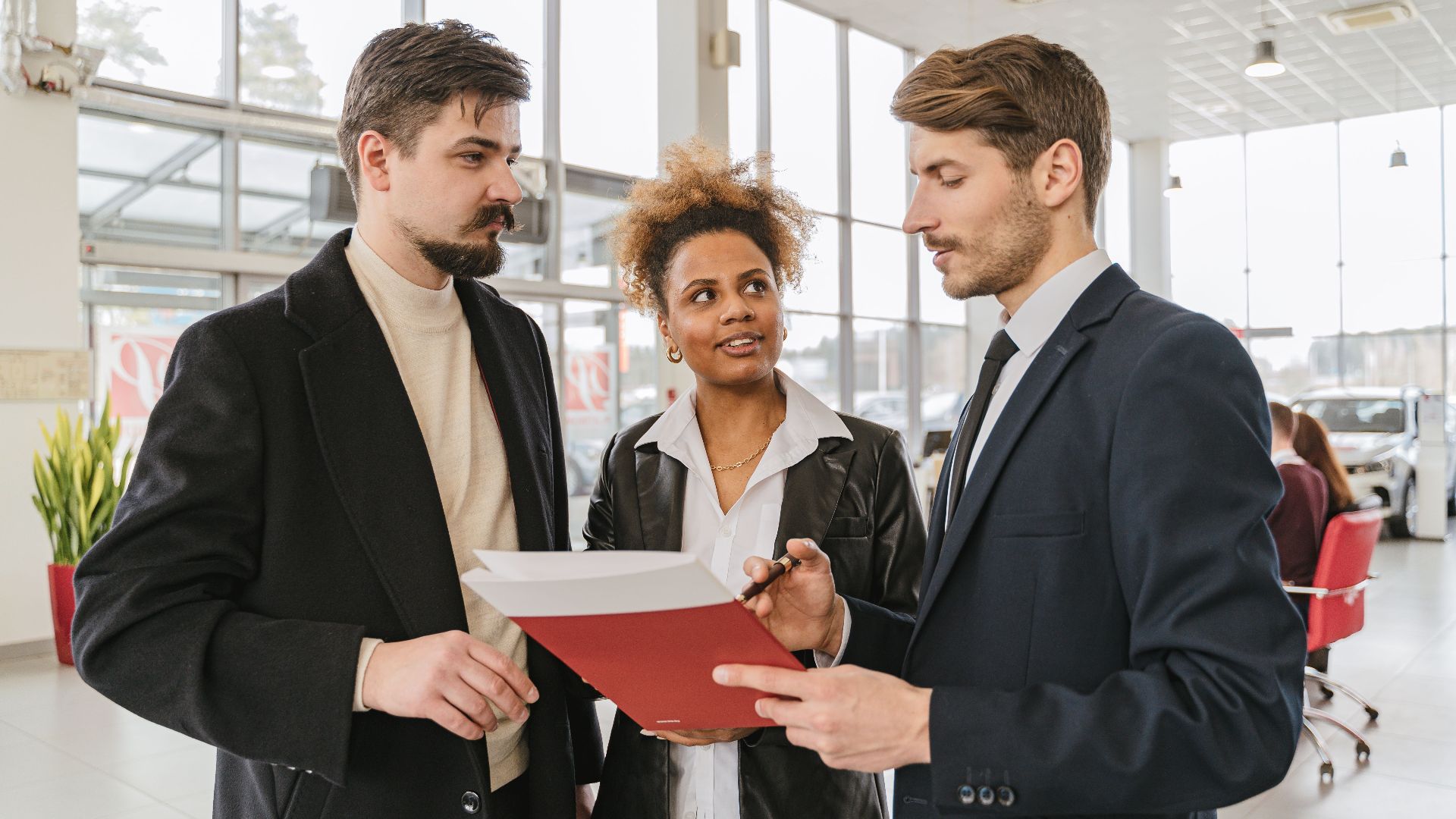 Business professionals discussing a car lease or purchase agreement in a showroom setting.