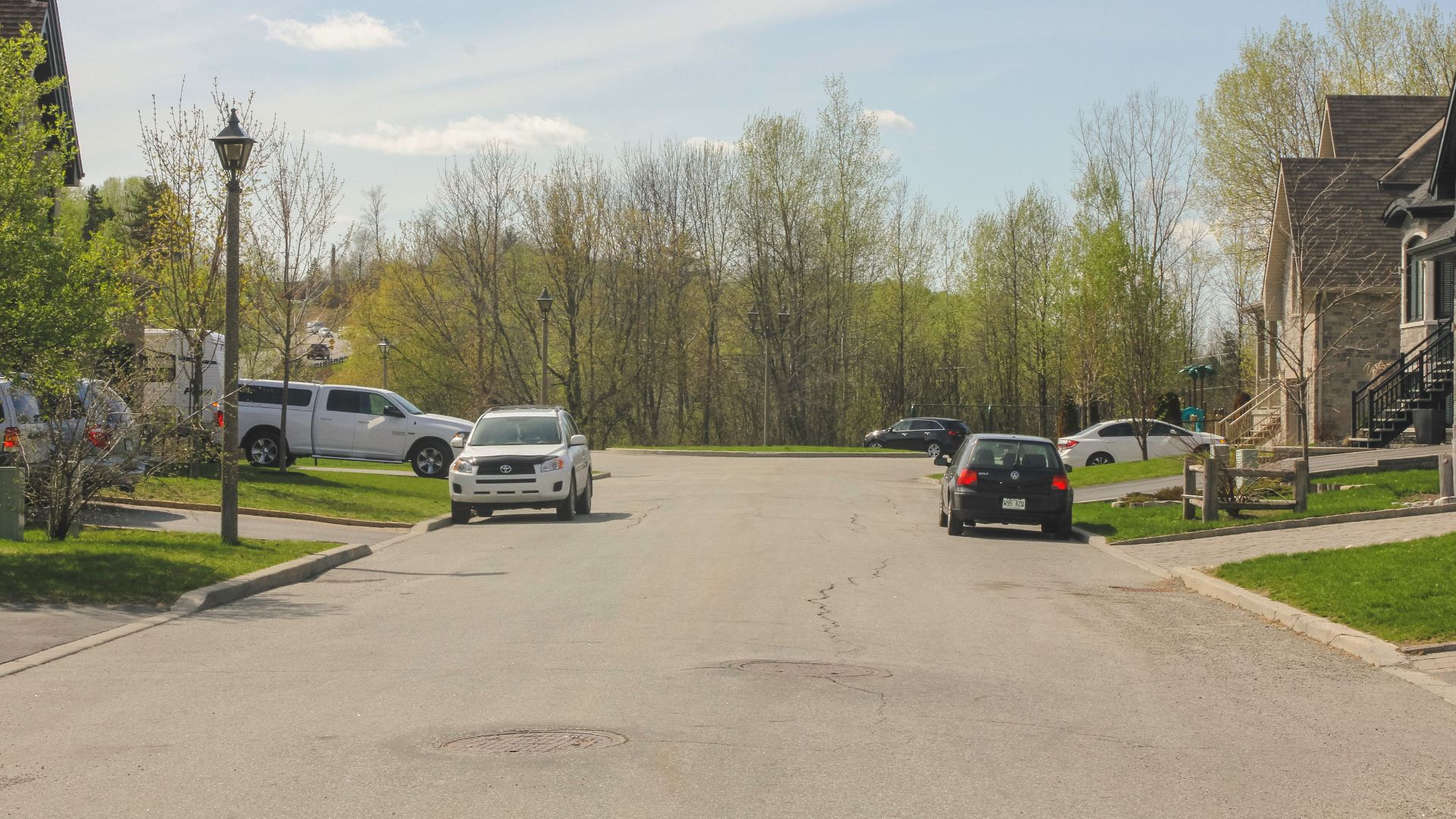 A peaceful suburban street in Gatineau, QC, Canada with parked cars and trees under a clear sky.