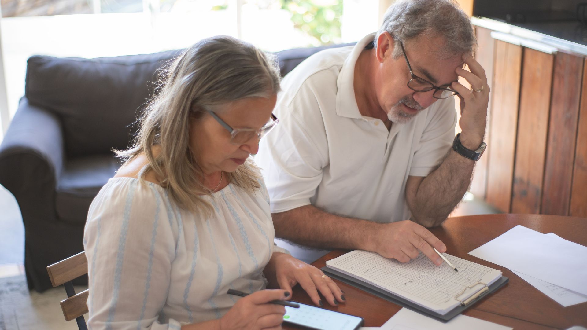Elderly couple reviewing bills and documents at home, focusing on finances and technology.