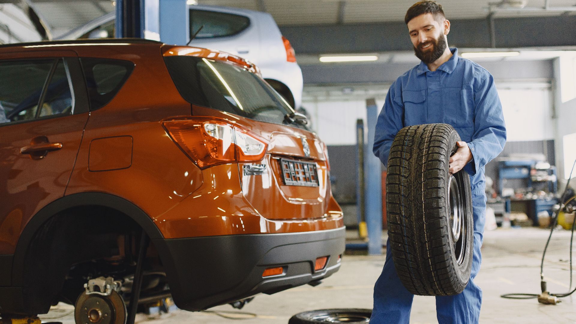 Mechanic holding a tire in a vehicle repair shop, showcasing automotive maintenance.
