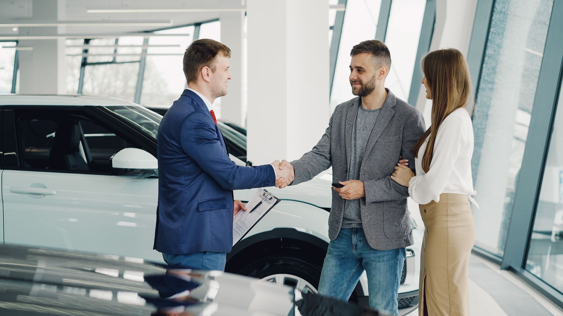 A couple completes a transaction with a salesman at a modern car dealership.