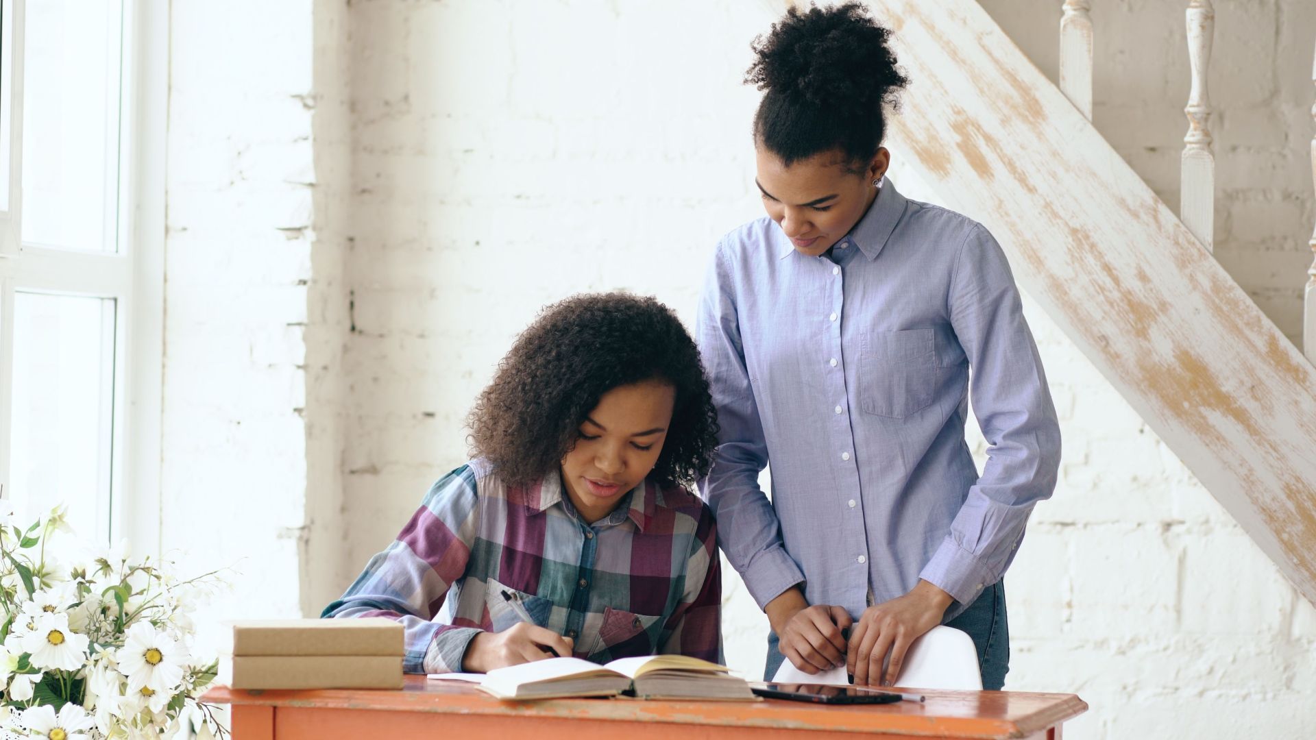 Mother helping daughter with homework at home in warm daylight.