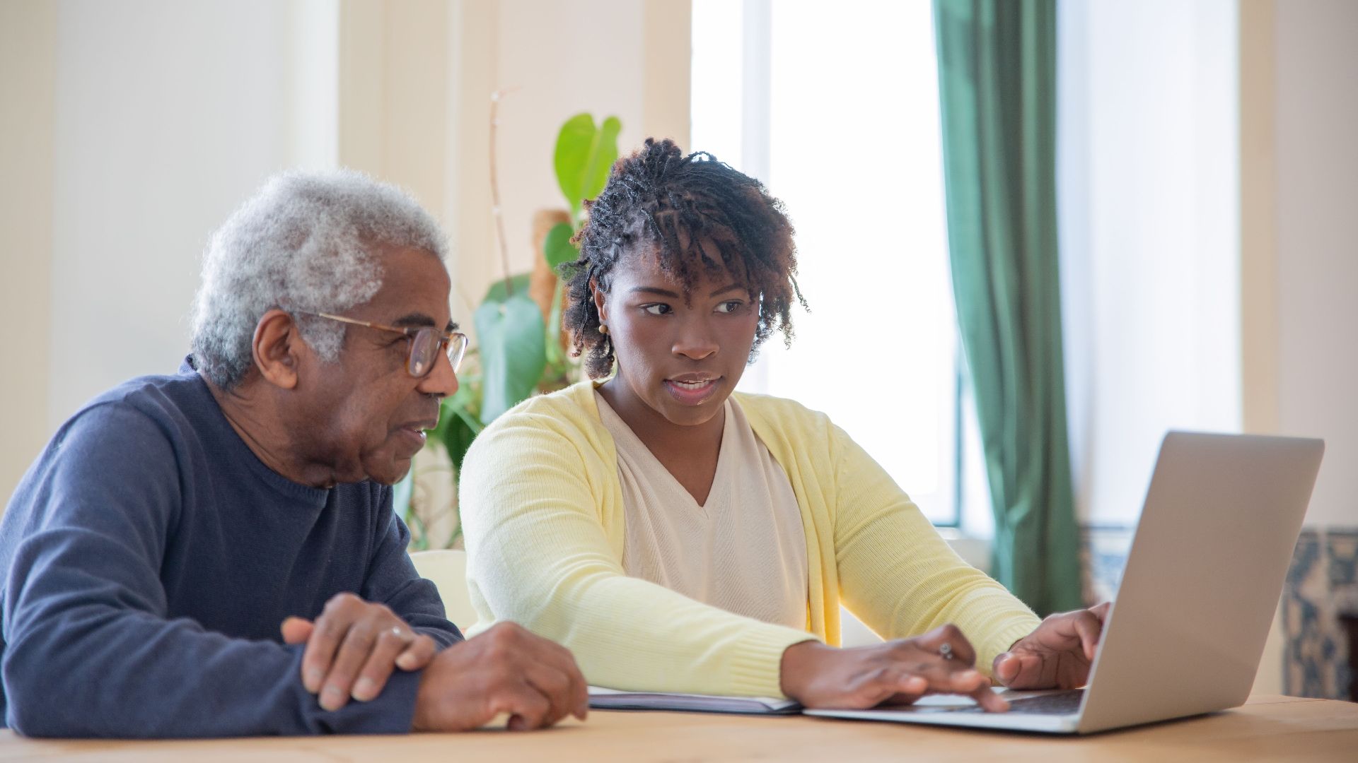Young woman assists an elderly man with laptop indoors, highlighting intergenerational tech support.