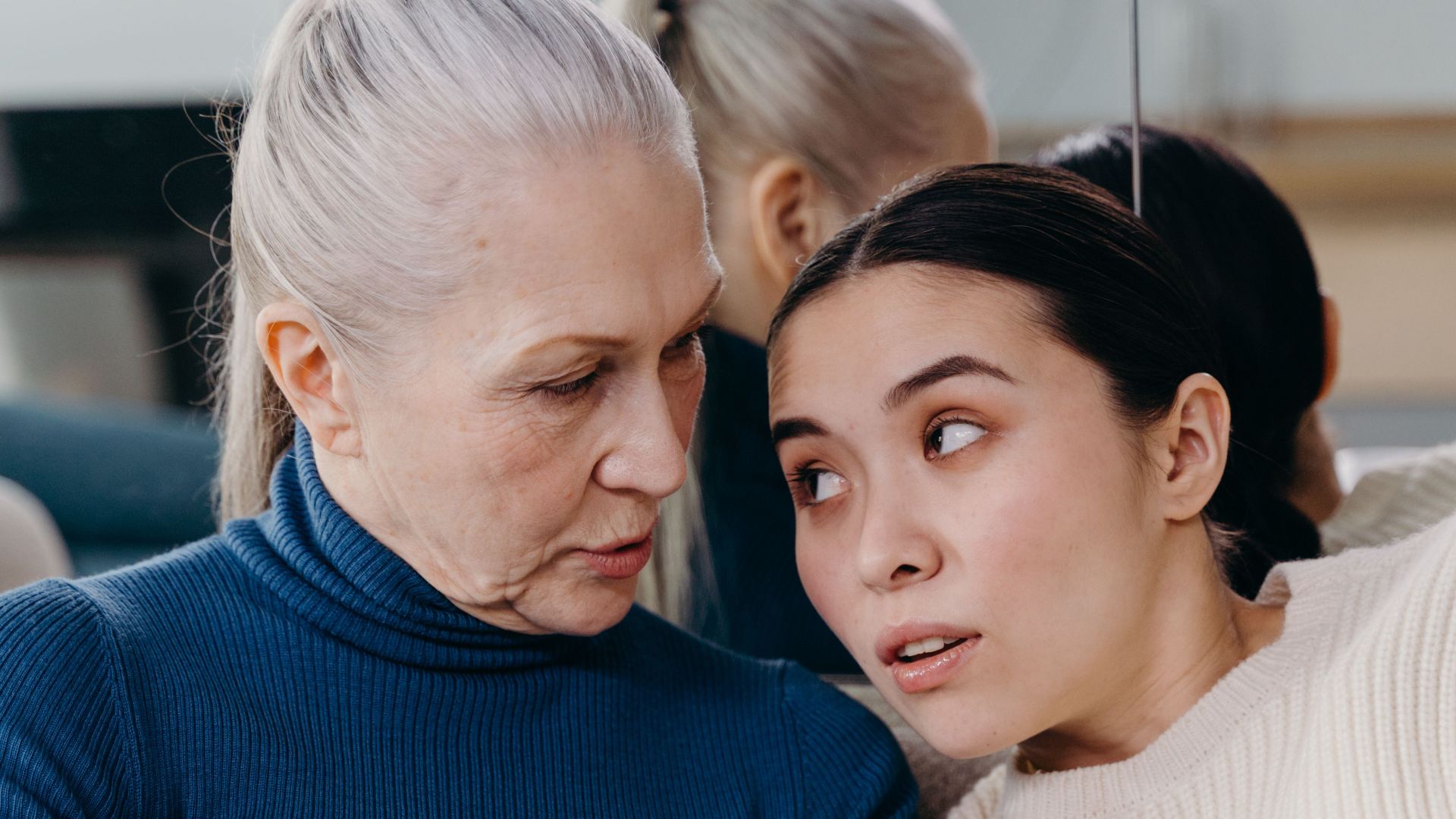An elderly woman and a young woman share a tender moment while reading together indoors.