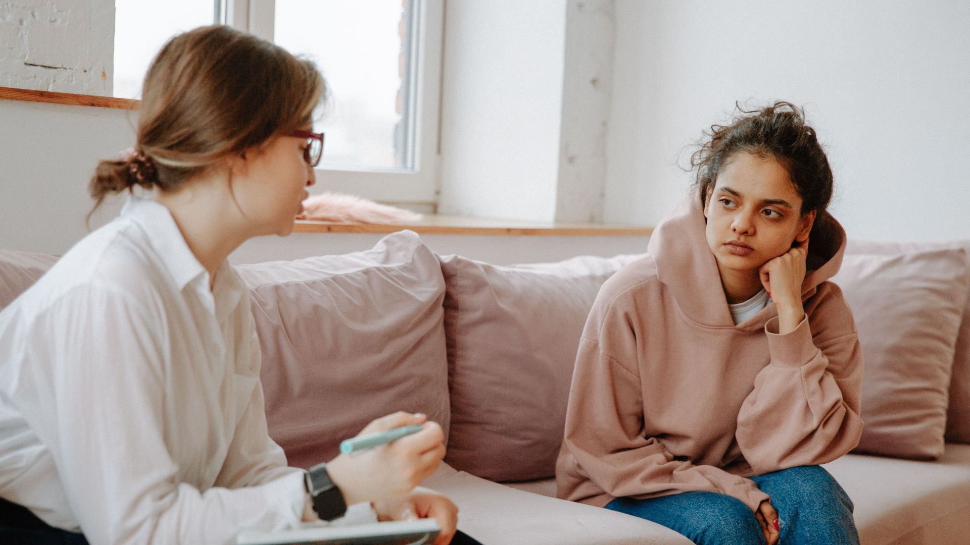 A teenager in a hoodie having a therapy session with a female therapist on a sofa.