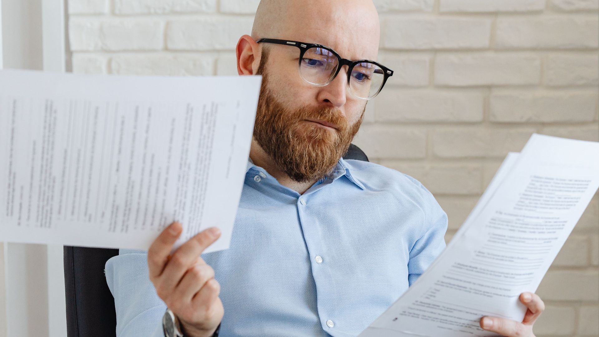 Bald bearded businessman reading financial documents in modern office setting.