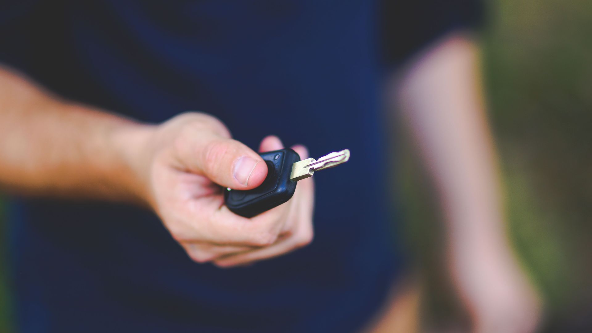 A hand holding a car key outdoors, emphasizing security and control.