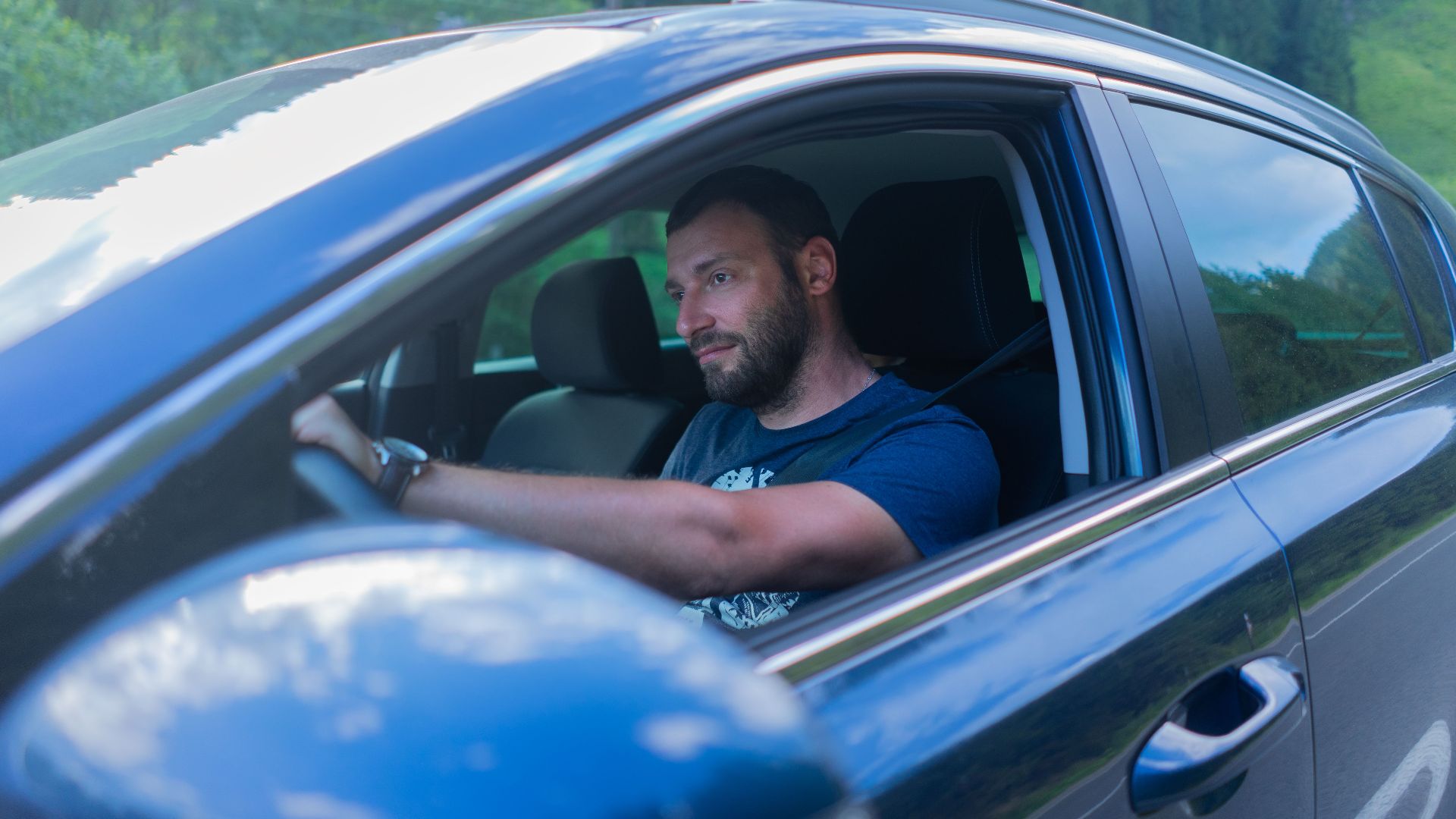 Bearded man enjoying a drive through lush green countryside on a sunny day.