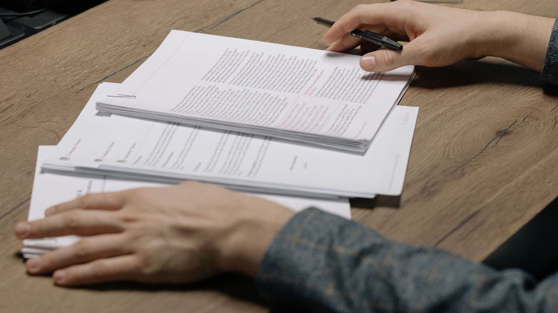 Close-up of a person reviewing documents with a pen at a modern office desk.